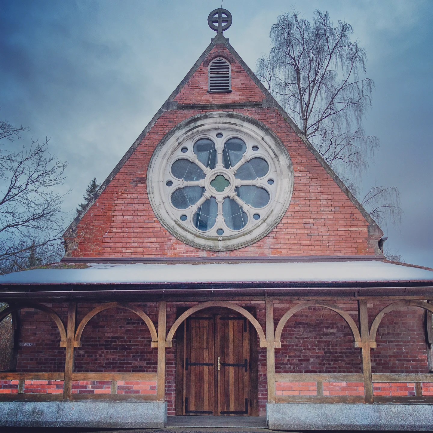 A red brick chapel with a large circular rose window and wooden porch in Mariánské Lázně.