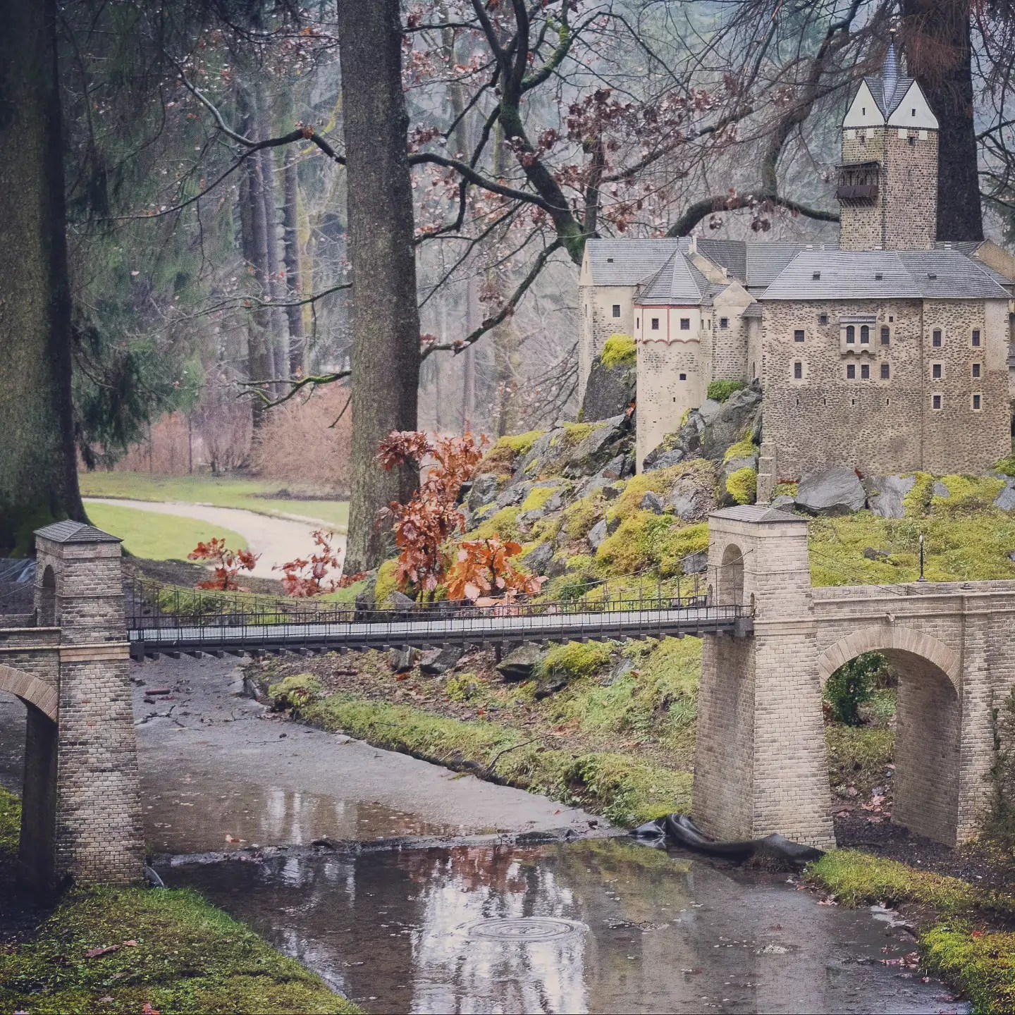 A detailed miniature stone castle with a tower and suspension bridge over a small stream in Park Boheminium in Mariánské Lázně.