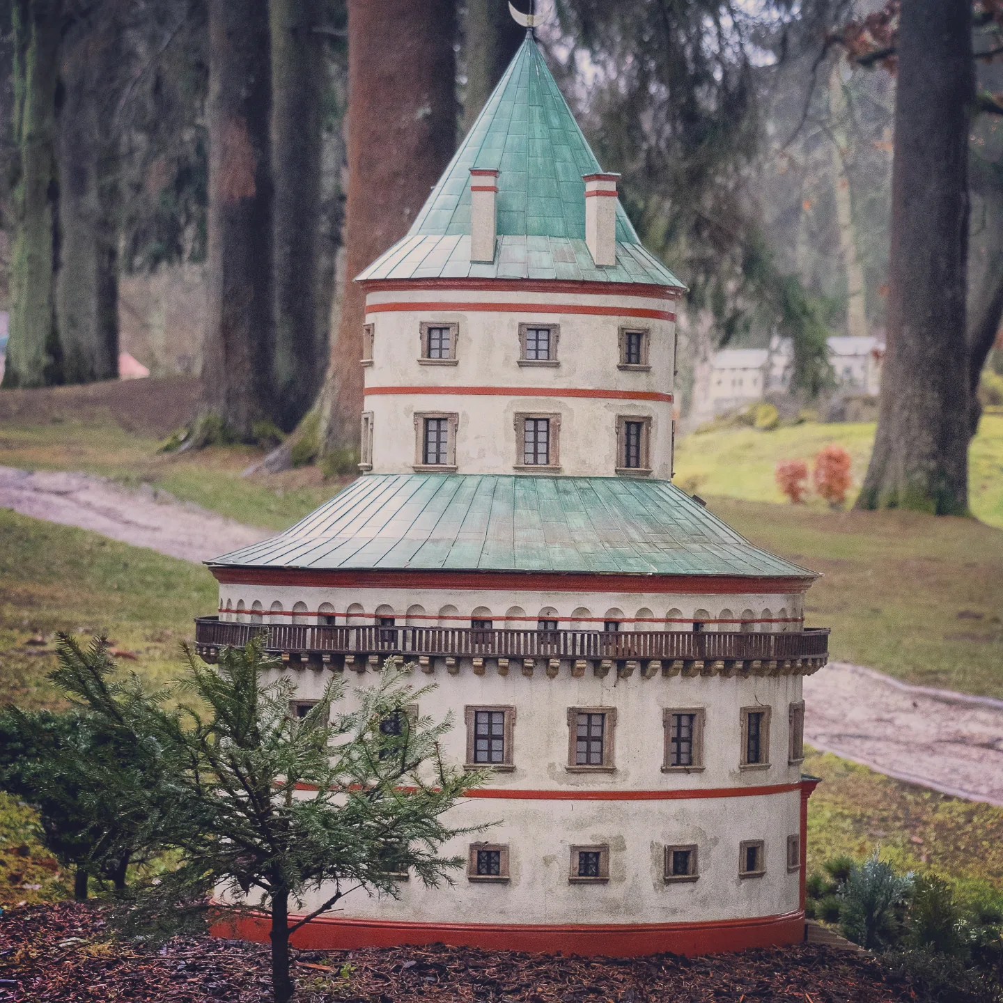 A circular miniature tower with a green roof and small windows displayed in Park Boheminium in Mariánské Lázně.