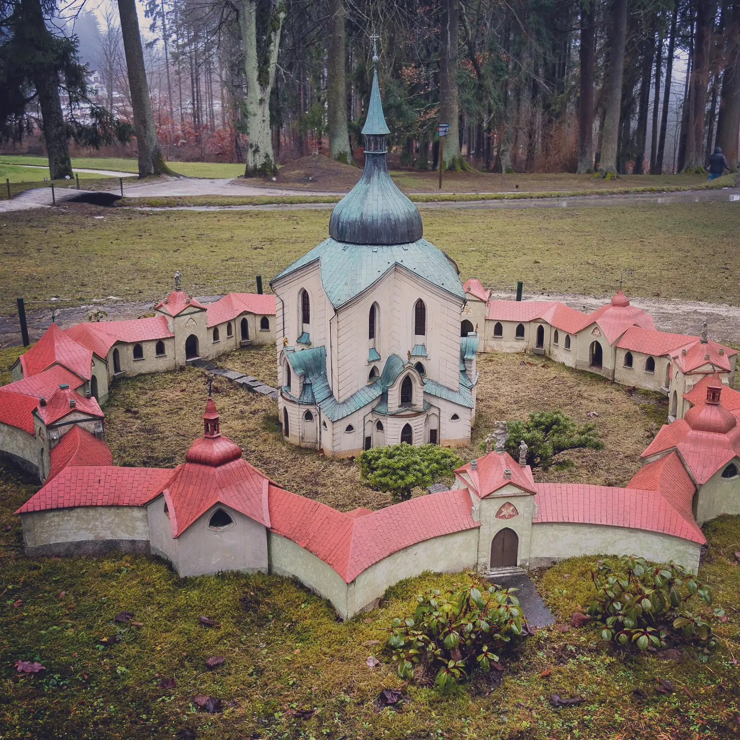 A miniature church with a green dome surrounded by red-roofed cloister buildings in Park Boheminium.