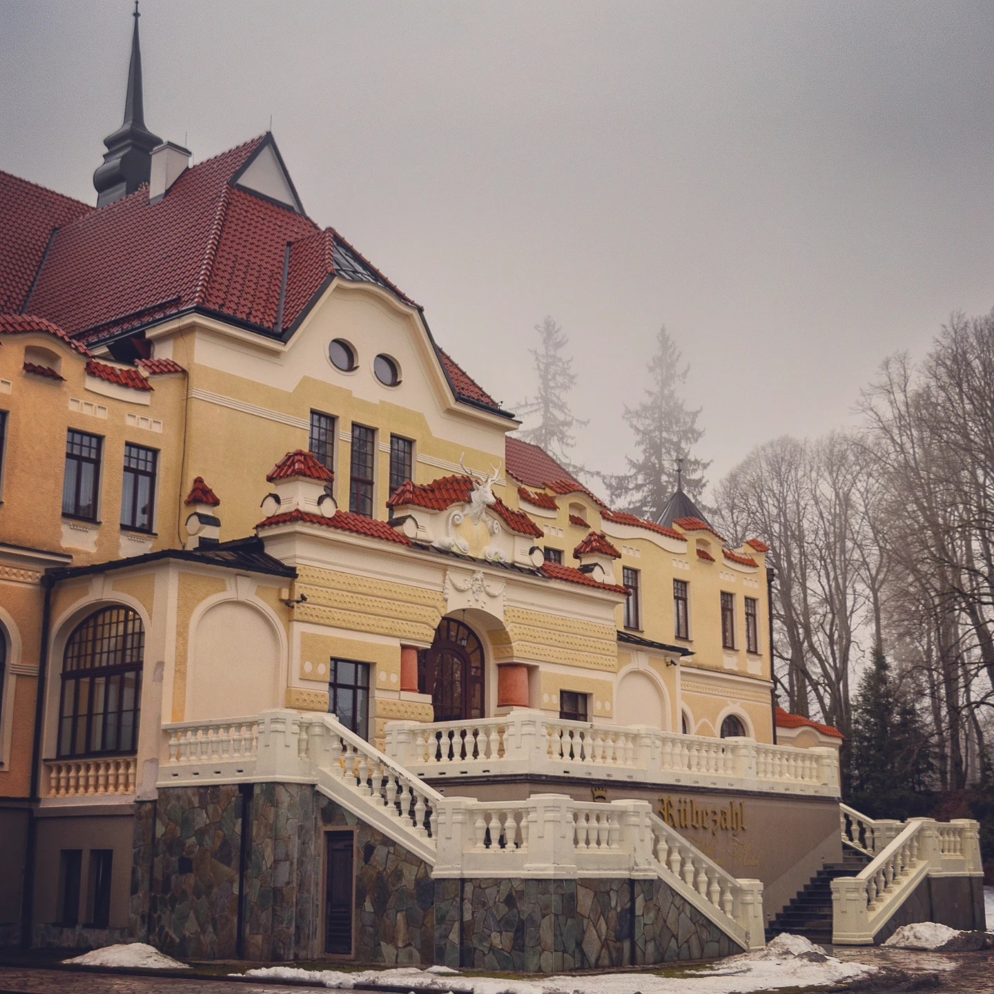 A historic yellow building with red tiled roofs and white staircases near Park Boheminium in Mariánské Lázně.