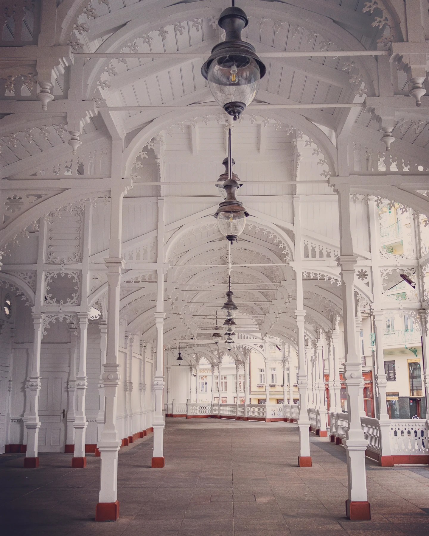 An ornate white wooden colonnade with decorative arches and hanging lanterns stretches into the distance.