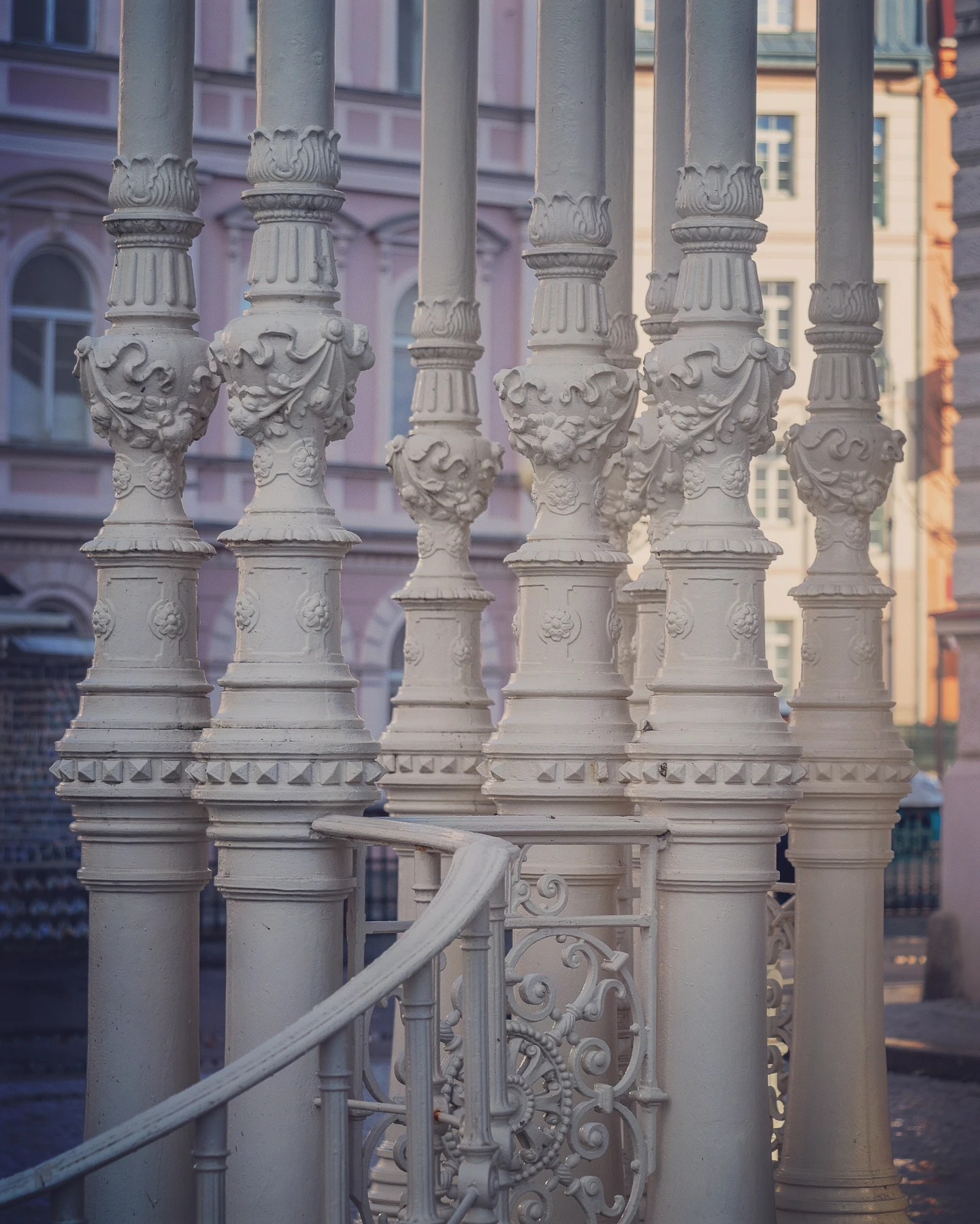 Close-up of white ornamental columns and curved railing details with pastel buildings blurred in the background.