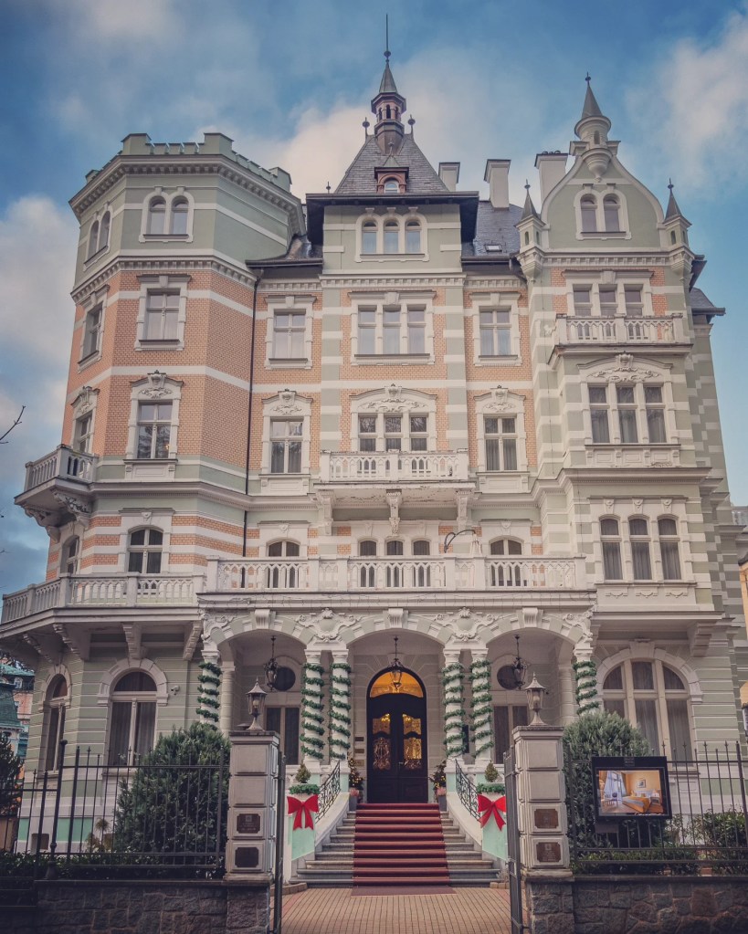 A grand historic villa with ornate balconies and decorative trim stands behind a gated staircase.