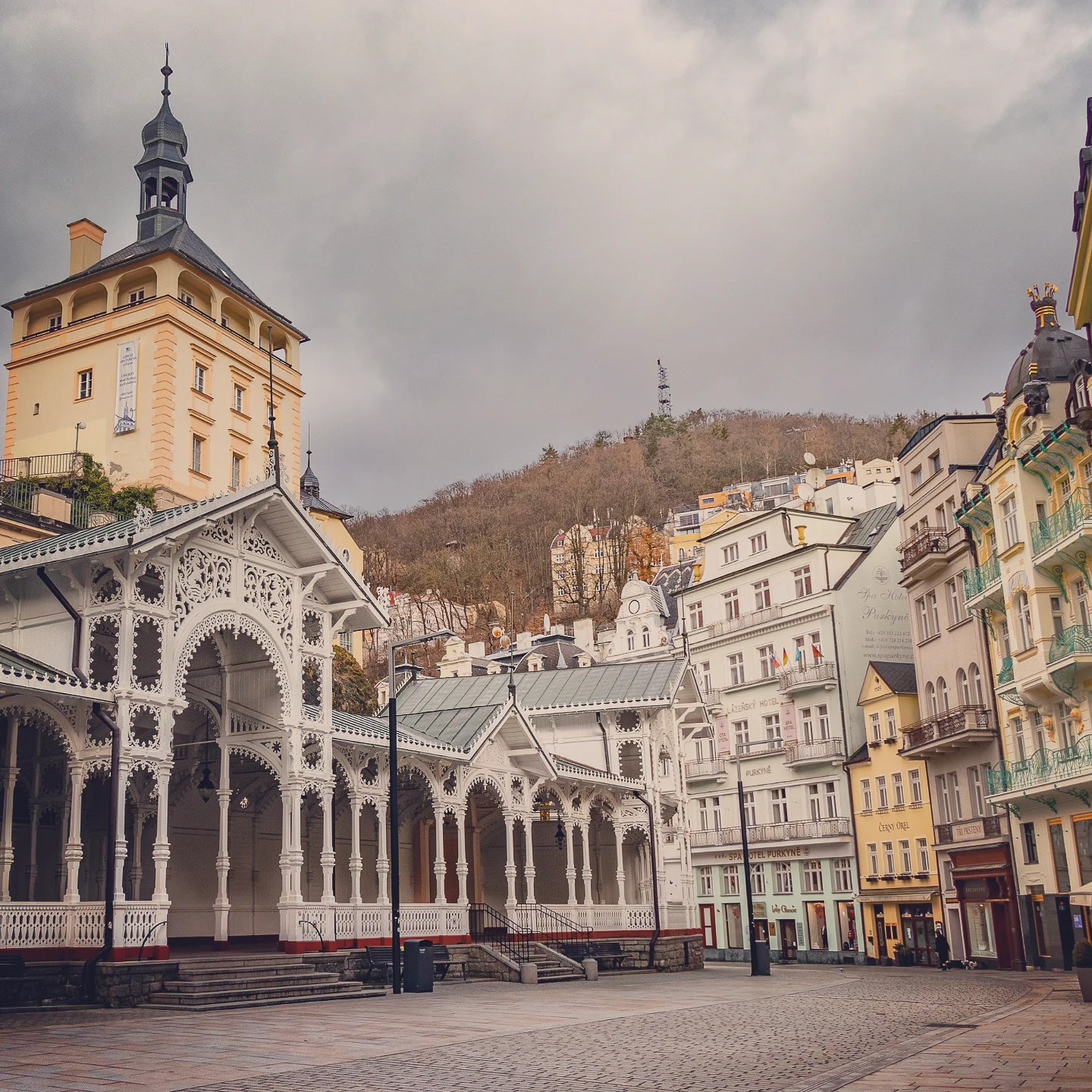 The Market Colonnade in Karlovy Vary with surrounding historic spa buildings and a hillside rising behind them.