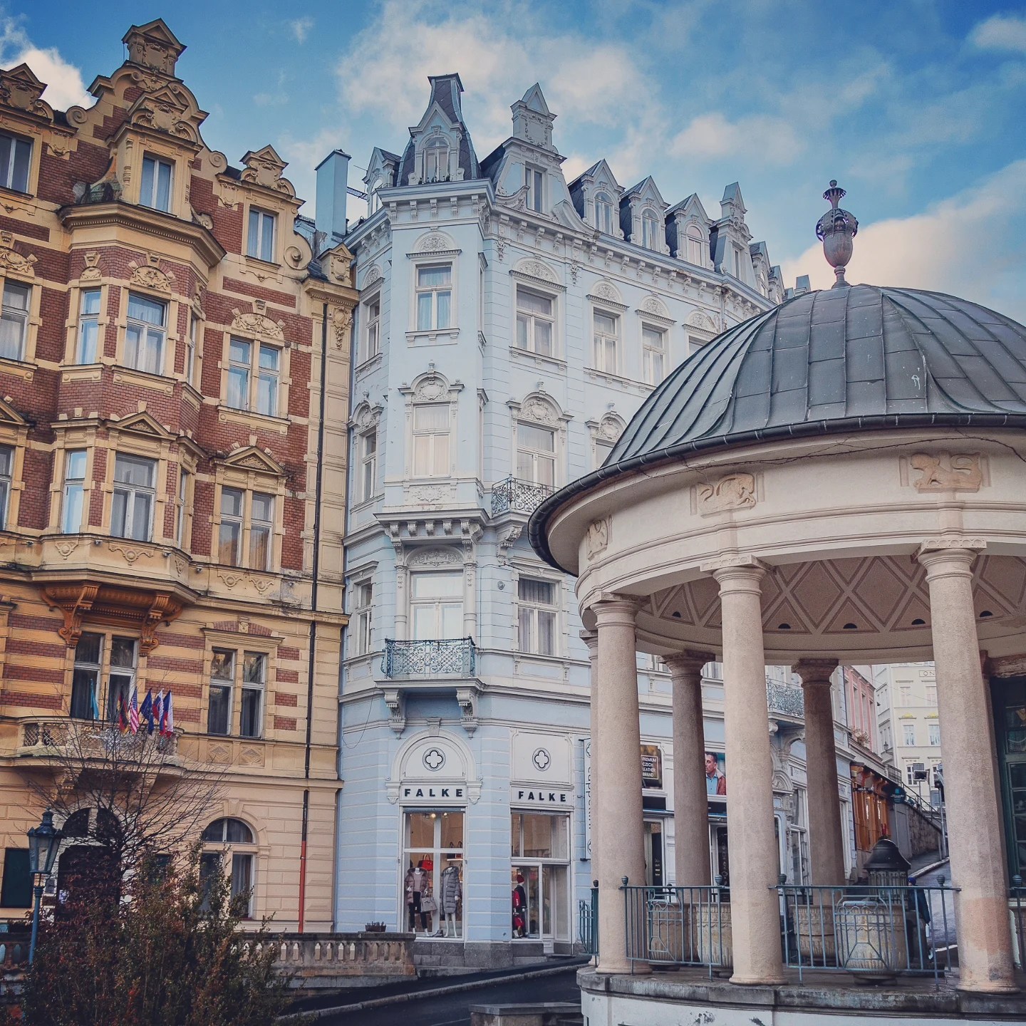 A round colonnaded pavilion in Karlovy Vary with ornate historic buildings behind it.