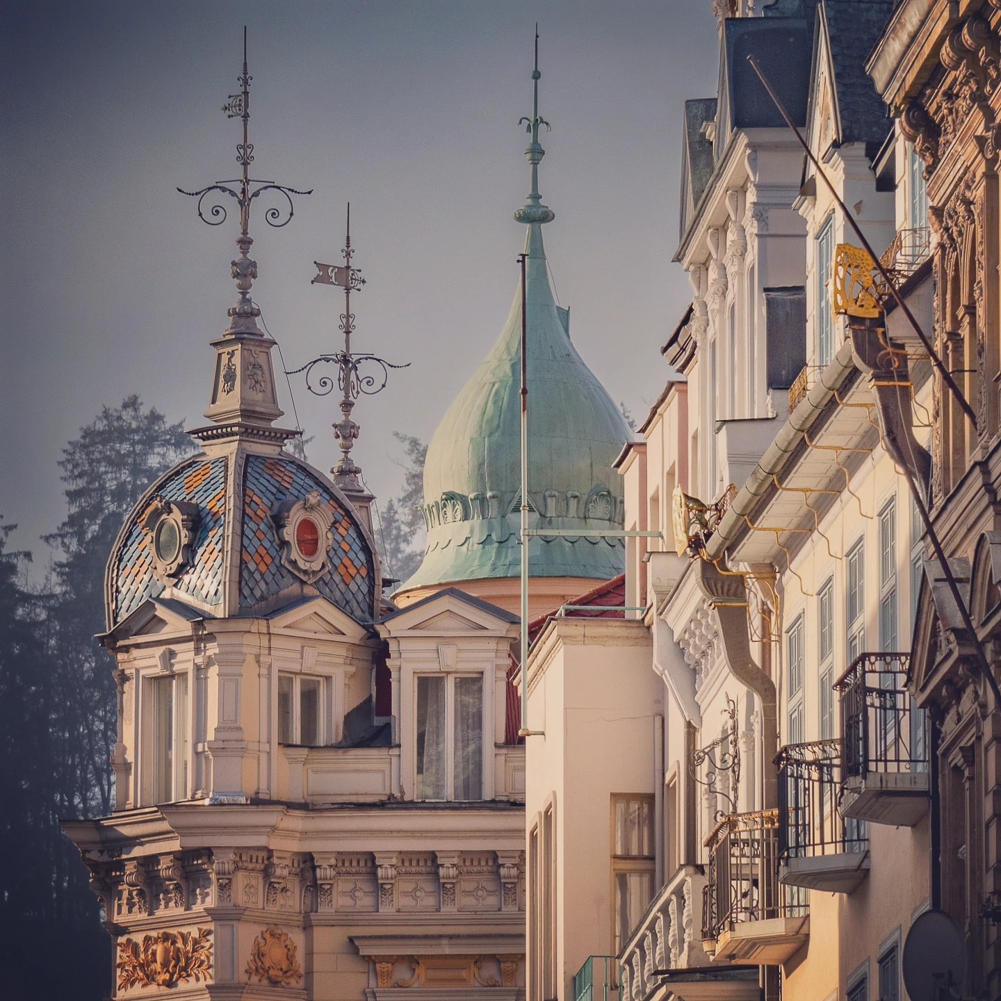 Decorative rooftops in Karlovy Vary featuring an ornate patterned dome, wrought iron finials, and a green onion-shaped dome rising behind pastel buildings.