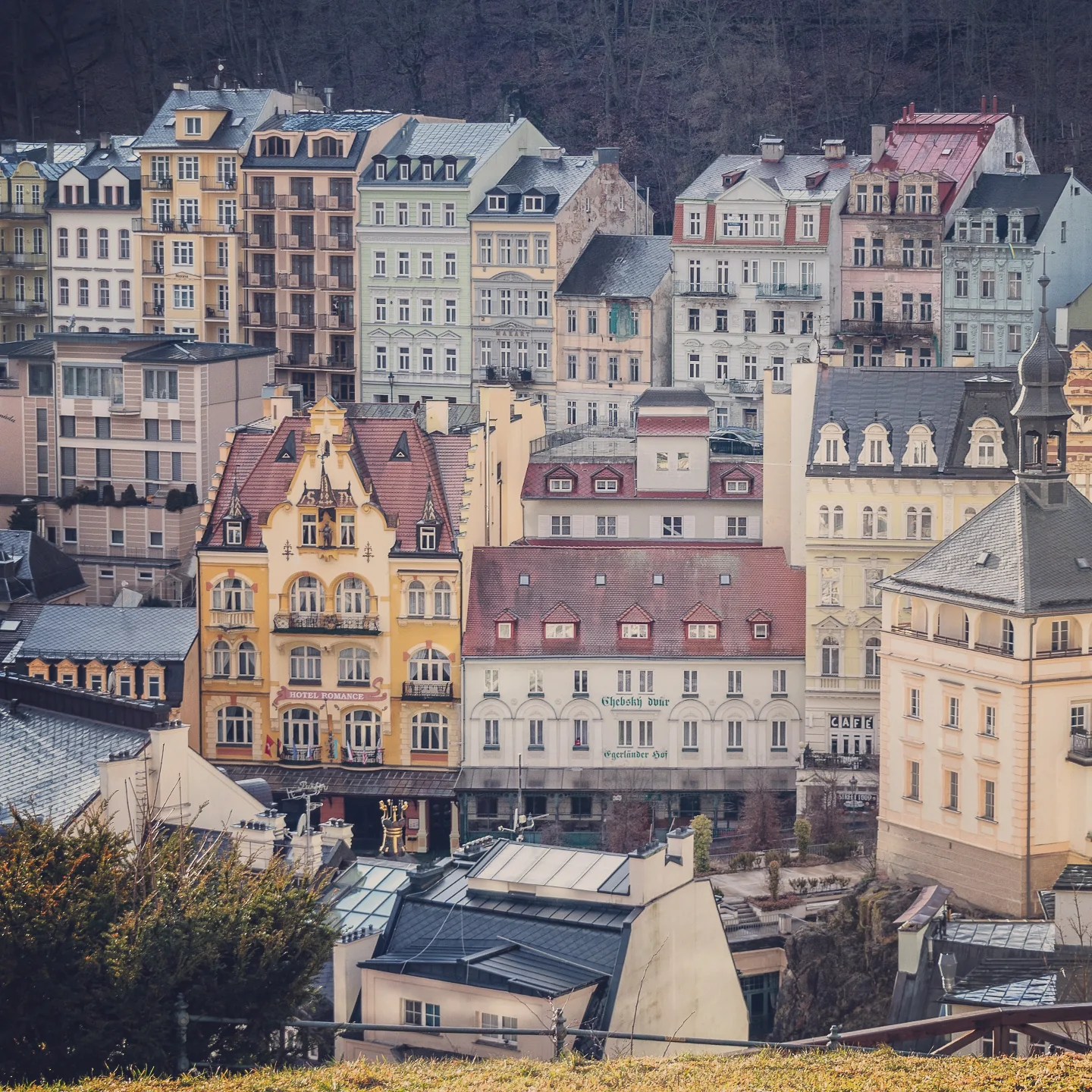 A view of Karlovy Vary’s historic center showing the yellow Hotel Romance building surrounded by pastel multi-story spa houses.