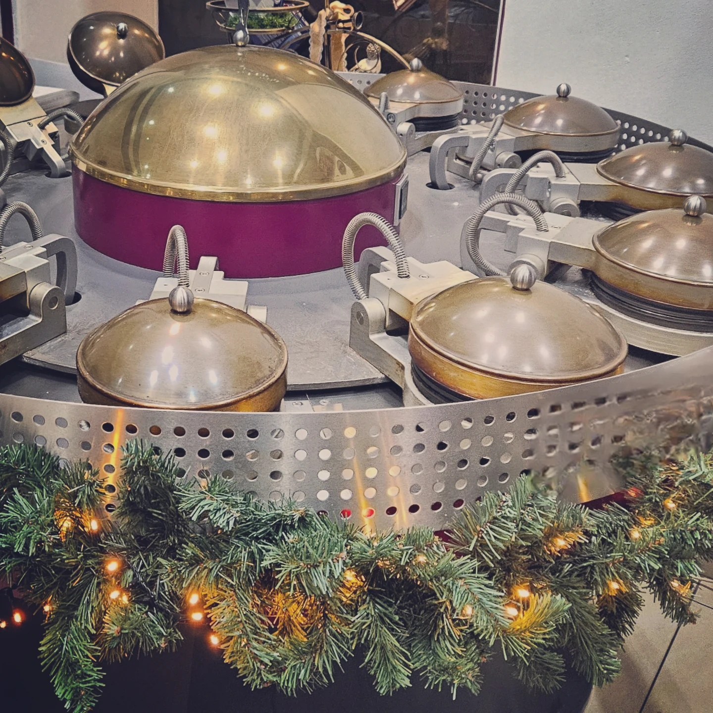 A round metal spa wafer press machine decorated with evergreen garland and small lights, used to make traditional Karlovy Vary wafers.
