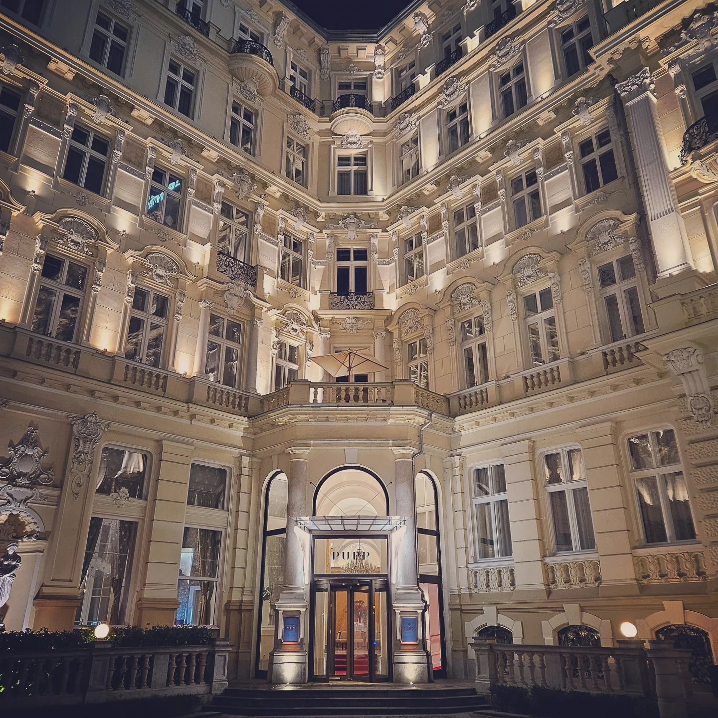 The illuminated historic façade and entrance of Grandhotel Pupp in Karlovy Vary at night, featuring ornate Baroque-style architecture and a grand doorway beneath a balcony.
