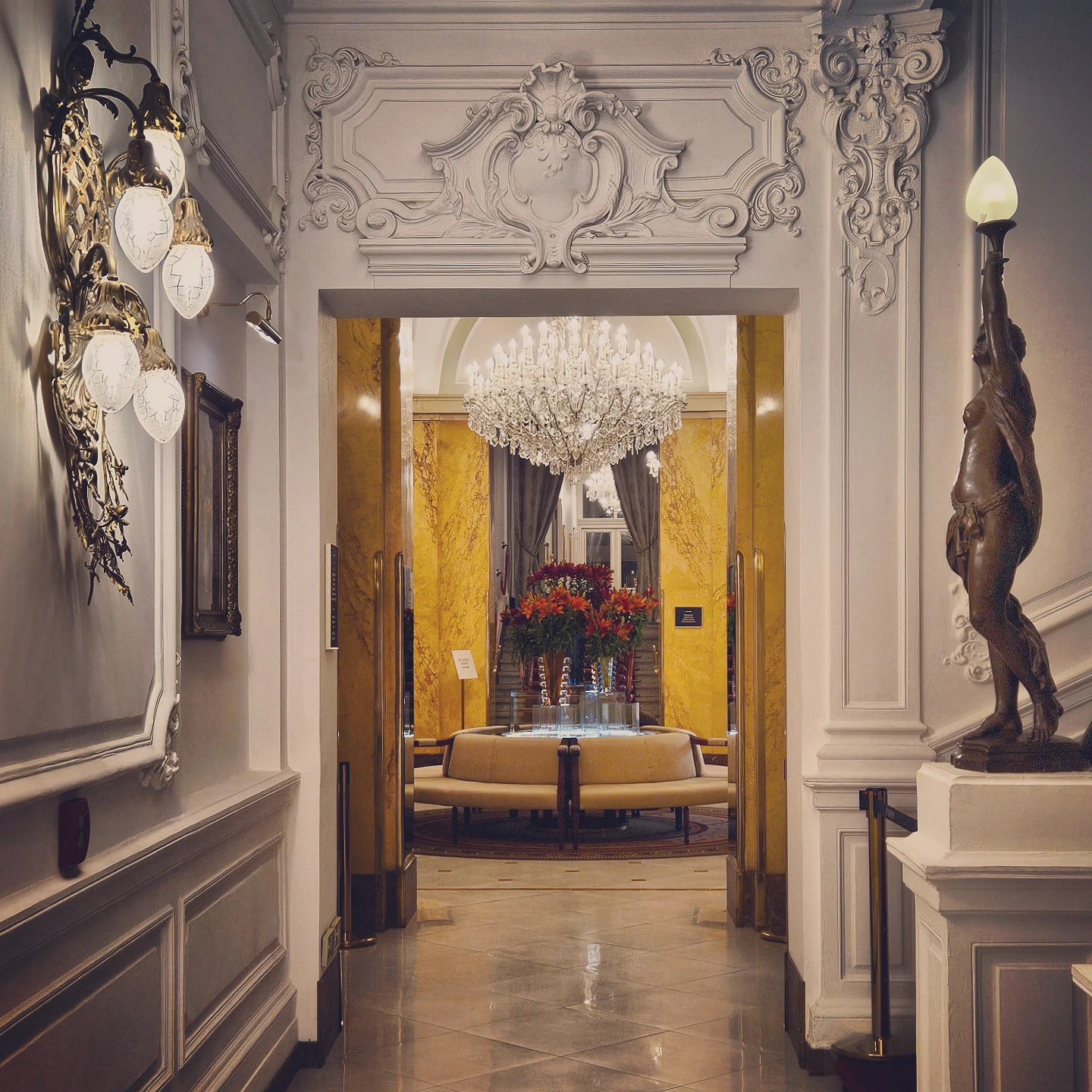 A view through an ornate doorway into a chandelier-lit lobby space at Grandhotel Pupp, with decorative moldings and wall sconces.