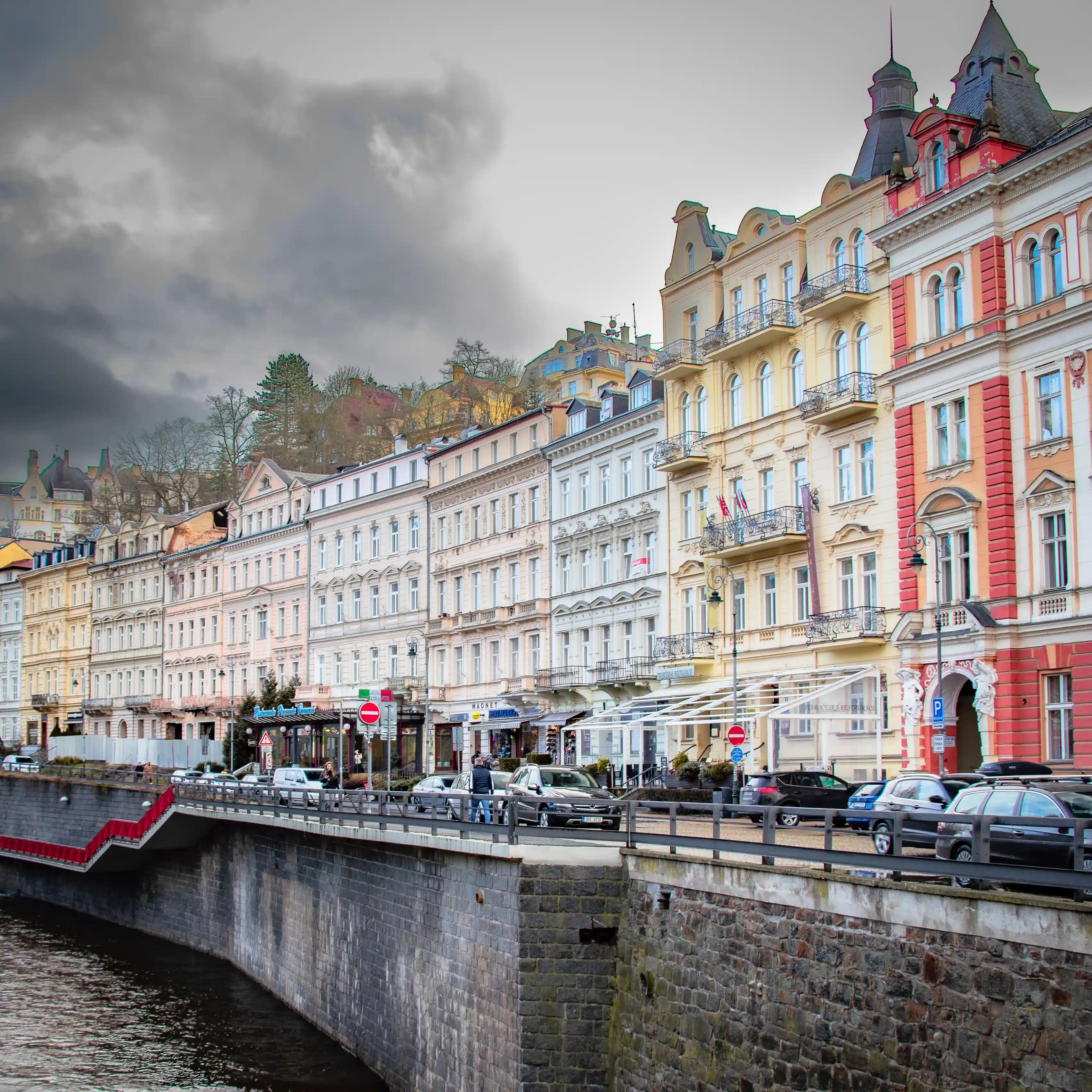 Colorful historic buildings line the Teplá River in Karlovy Vary, with Staročeská Restaurace visible among the pastel façades.