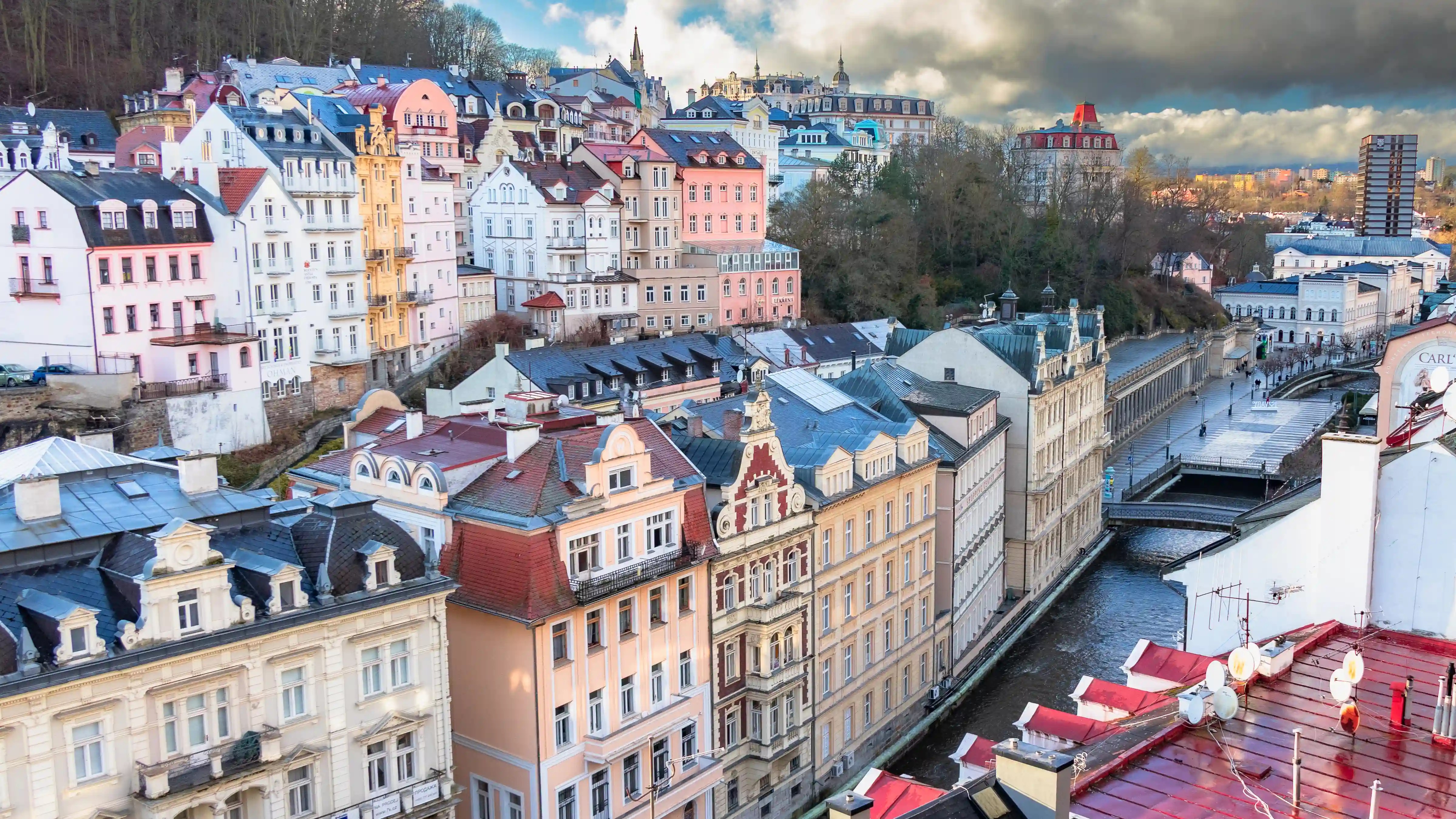 An elevated view of pastel buildings in Karlovy Vary with the Teplá River running through the center and the Mill Colonnade visible along the water.
