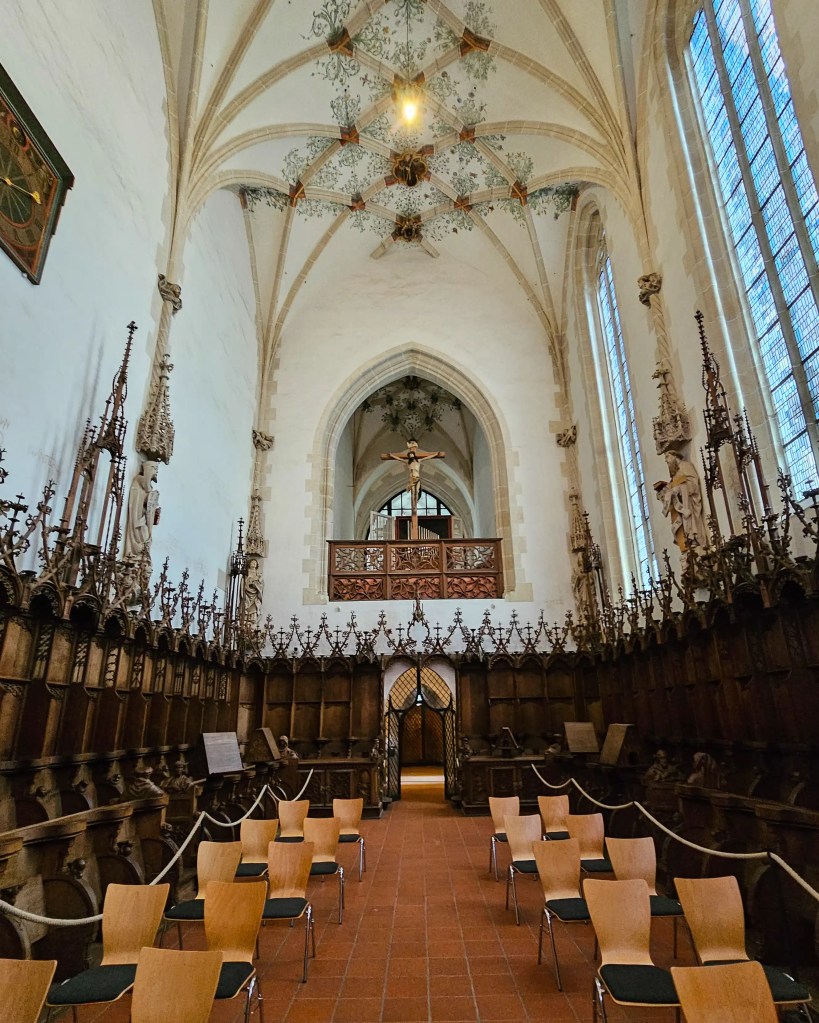 The interior choir of Kloster Blaubeuren shows carved wooden stalls beneath a high vaulted ceiling with decorative details.