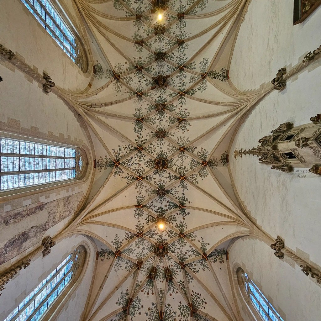 The vaulted ceiling of Kloster Blaubeuren’s church features painted floral patterns between intersecting Gothic ribs and tall arched windows.