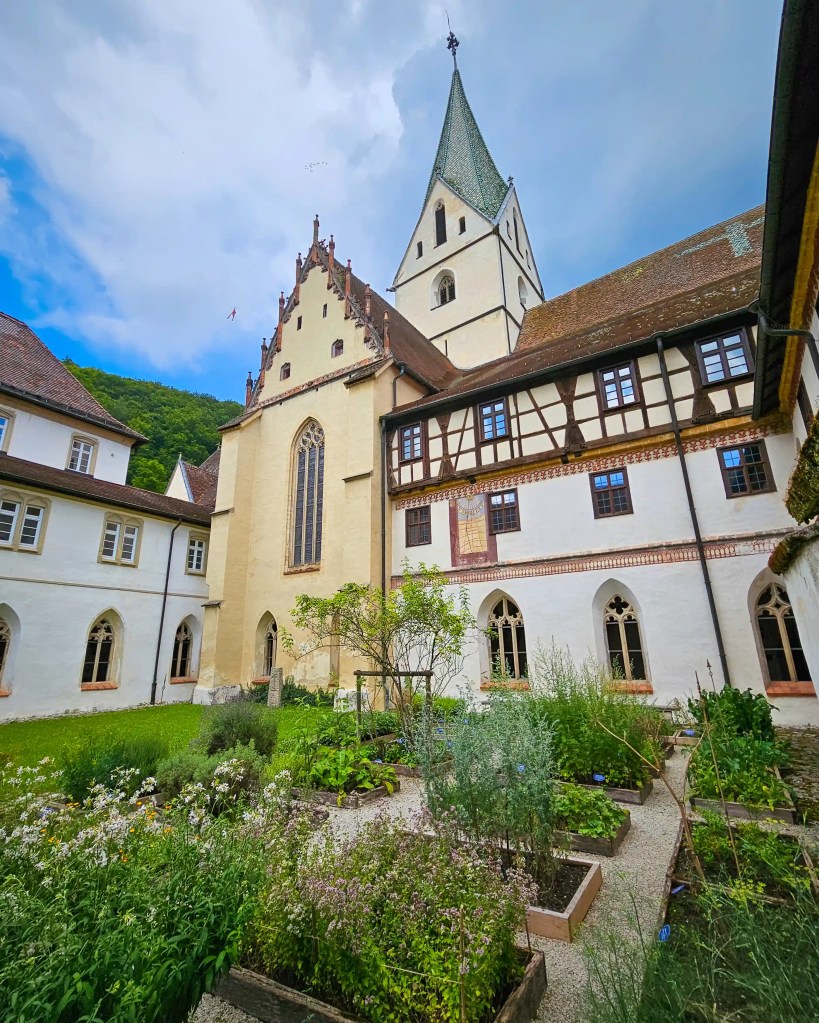The courtyard of Kloster Blaubeuren with a herb garden in raised beds and the monastery church rising behind it.