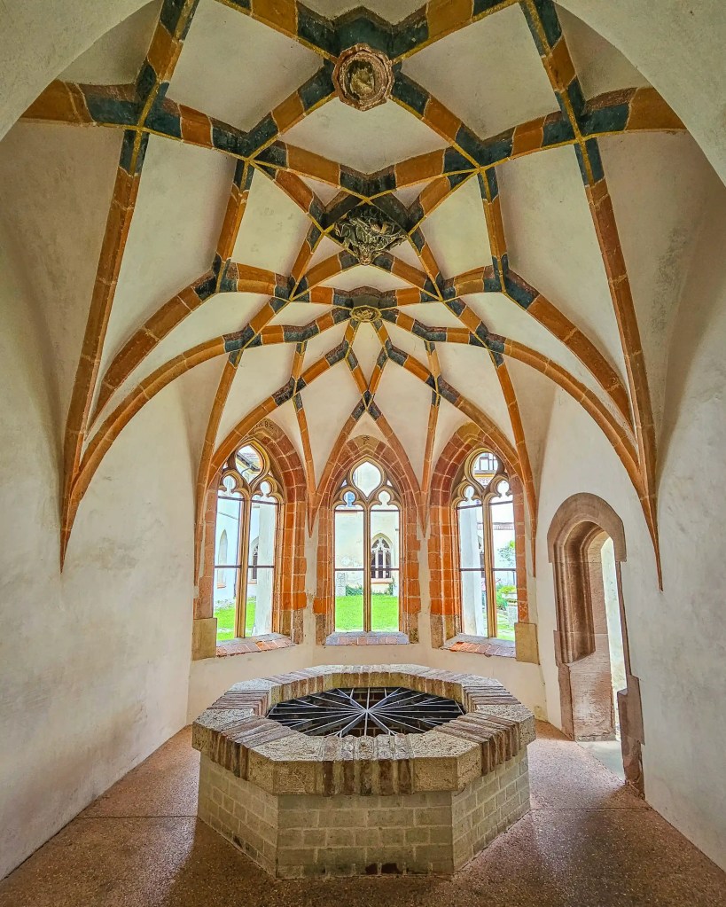 A small vaulted chapel-like room inside Kloster Blaubeuren features pointed Gothic windows and an octagonal stone structure in the center.