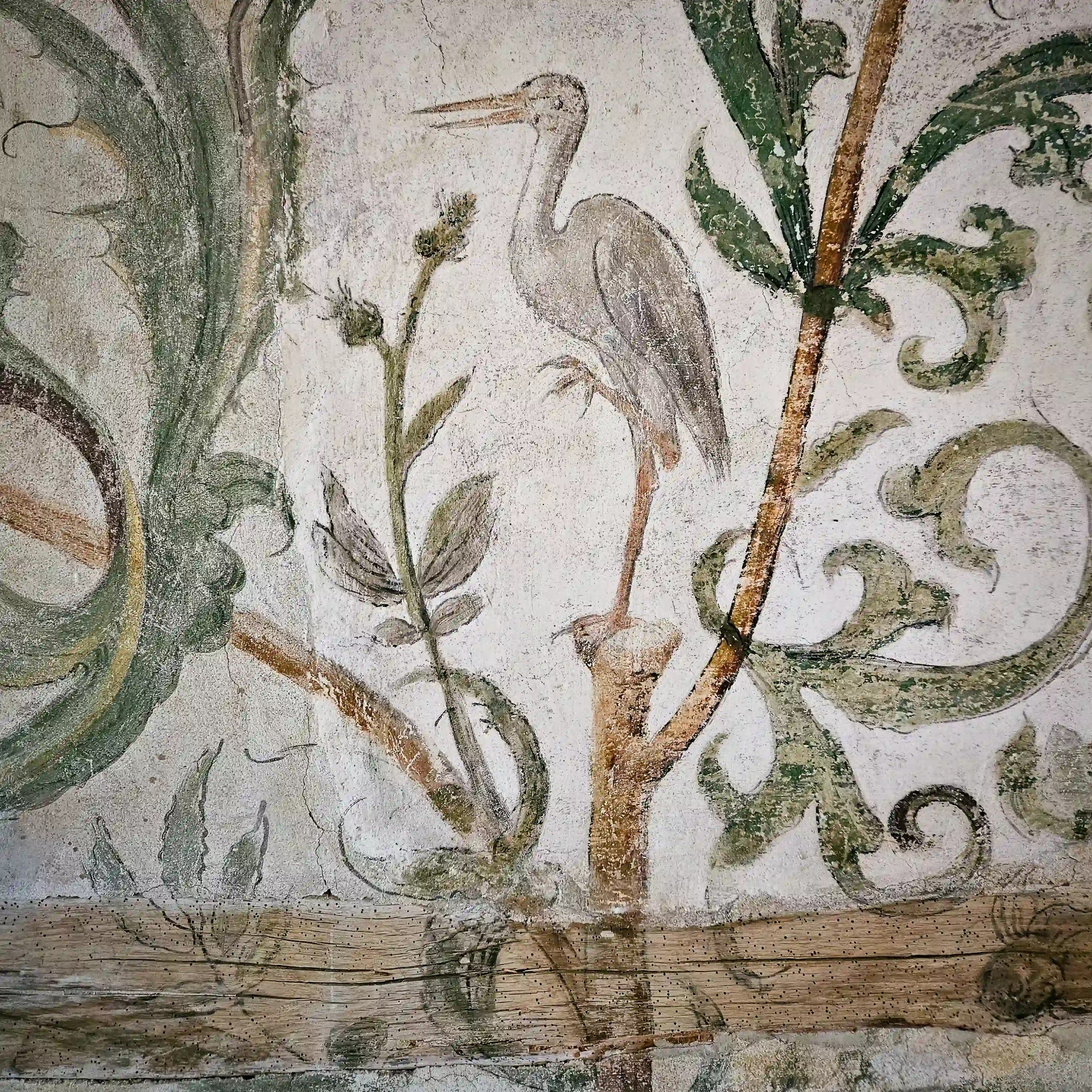 A painted medieval wall fresco of a tall white bird standing among vines decorates a plaster wall.