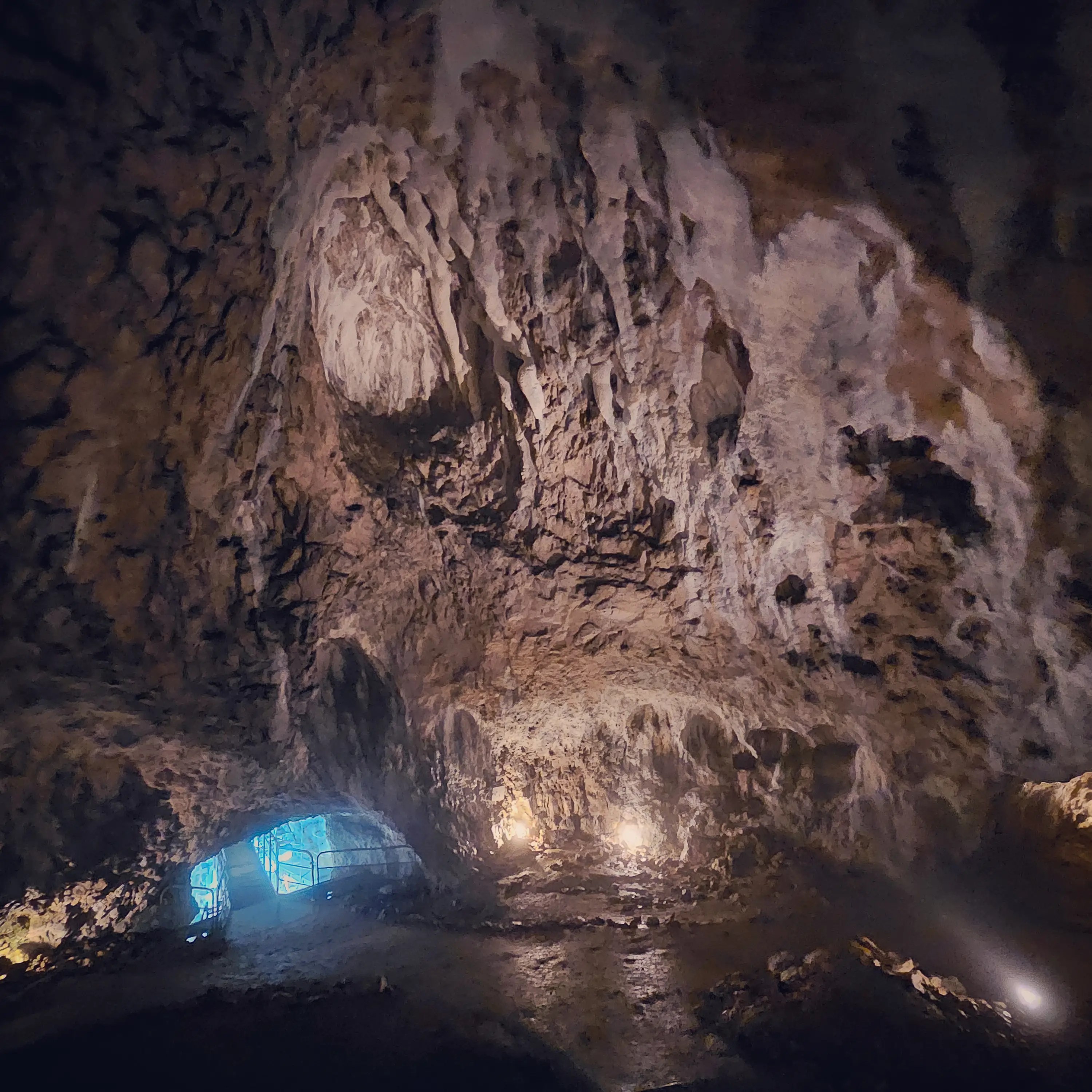 A wide view inside Hohle Fels Cave shows textured rock walls illuminated by small lights, with a blue-lit opening visible in the distance.