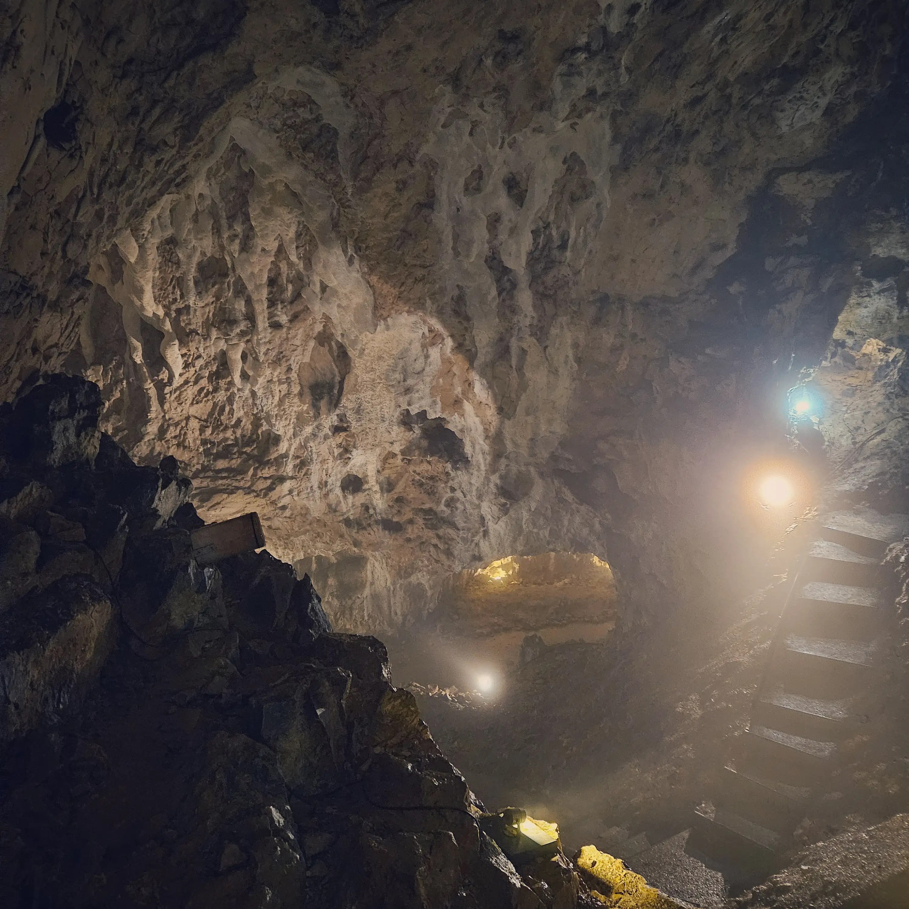 A dimly lit section of Hohle Fels Cave shows steep steps leading upward beside rough rock walls illuminated by warm spotlights.