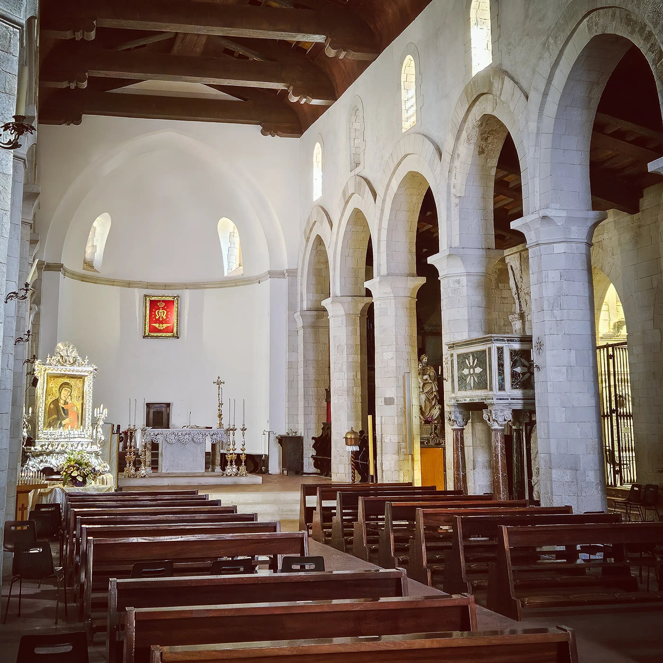 Rows of wooden pews facing an altar inside a church with stone arches and a wooden ceiling.