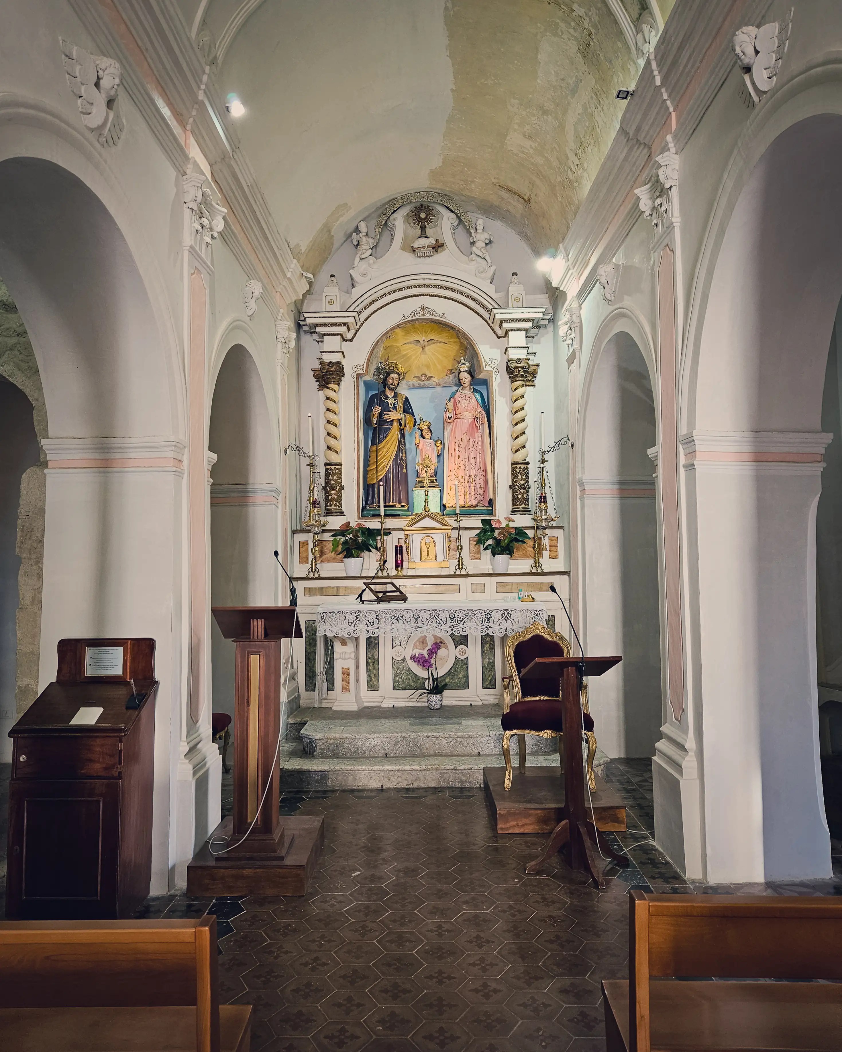 Small church interior with an altar, religious statues, arched walls, and wooden pews.