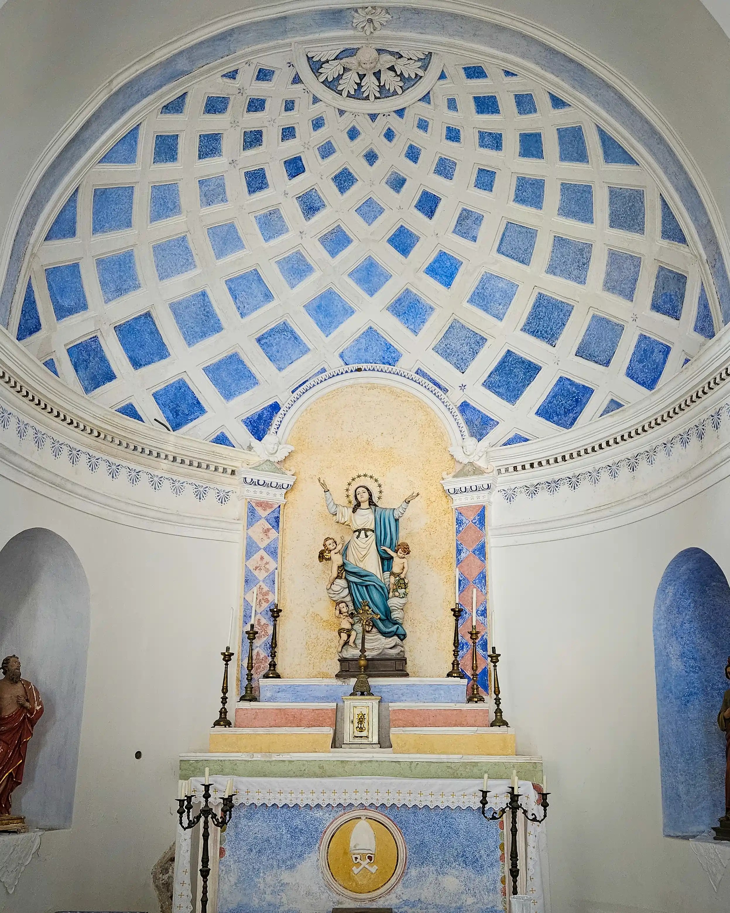 A church apse with a blue coffered dome ceiling above an altar featuring a statue of the Virgin Mary with two angels.