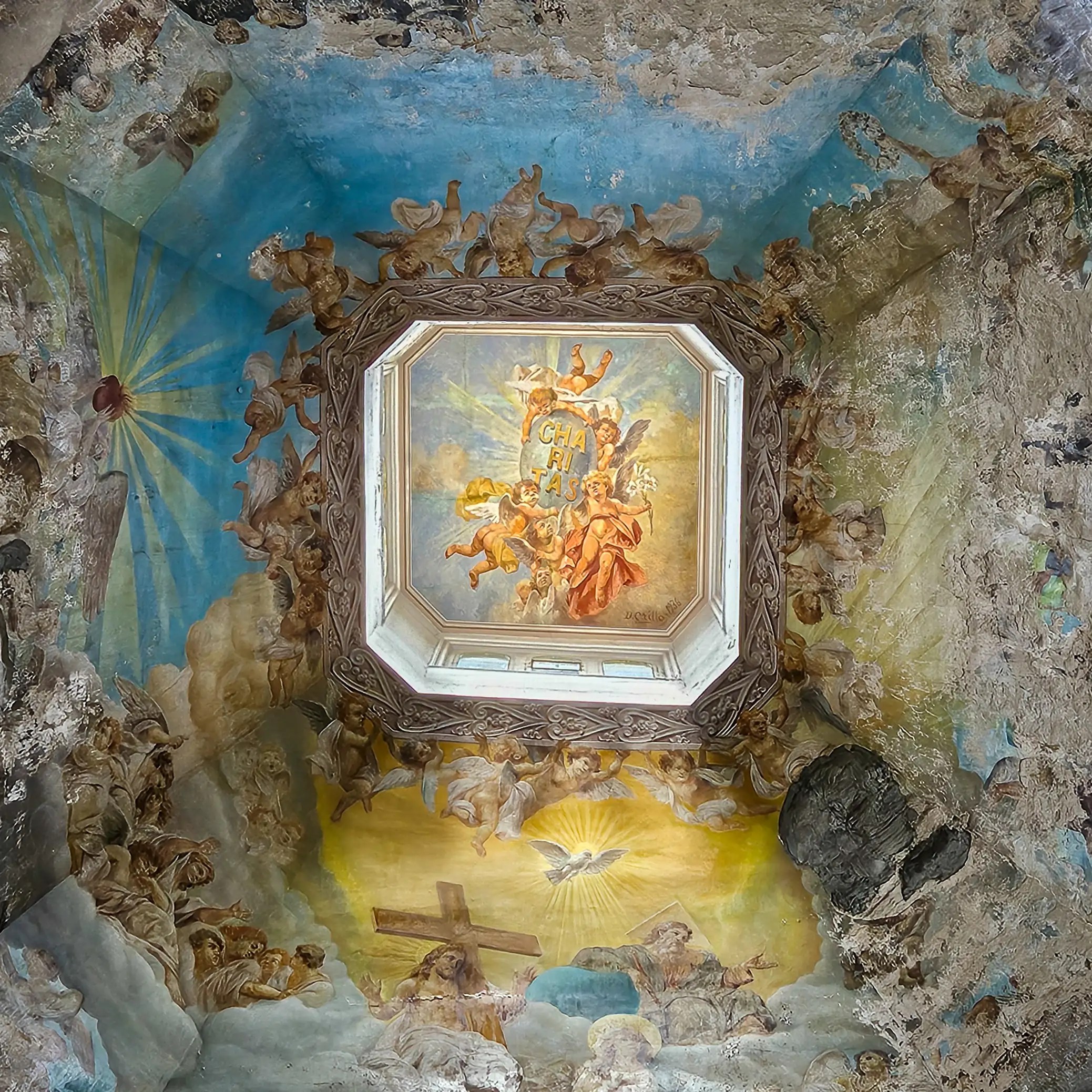 A decorative ceiling with a painted religious scene surrounded by figures and clouds, framed by an octagonal opening.