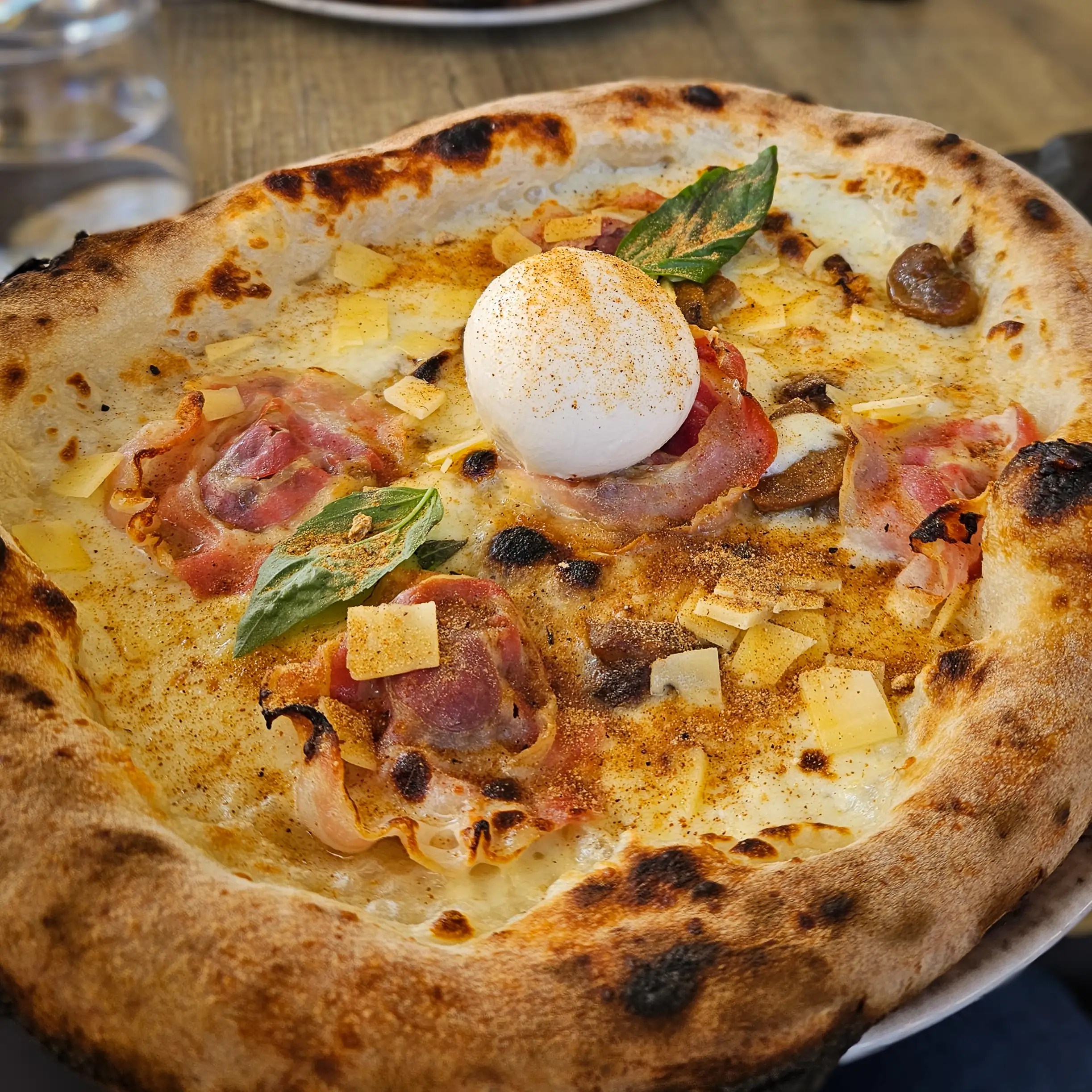 A pizza topped with melted cheese, slices of cured meat, mushrooms, basil leaves, and a round white cheese in the center.