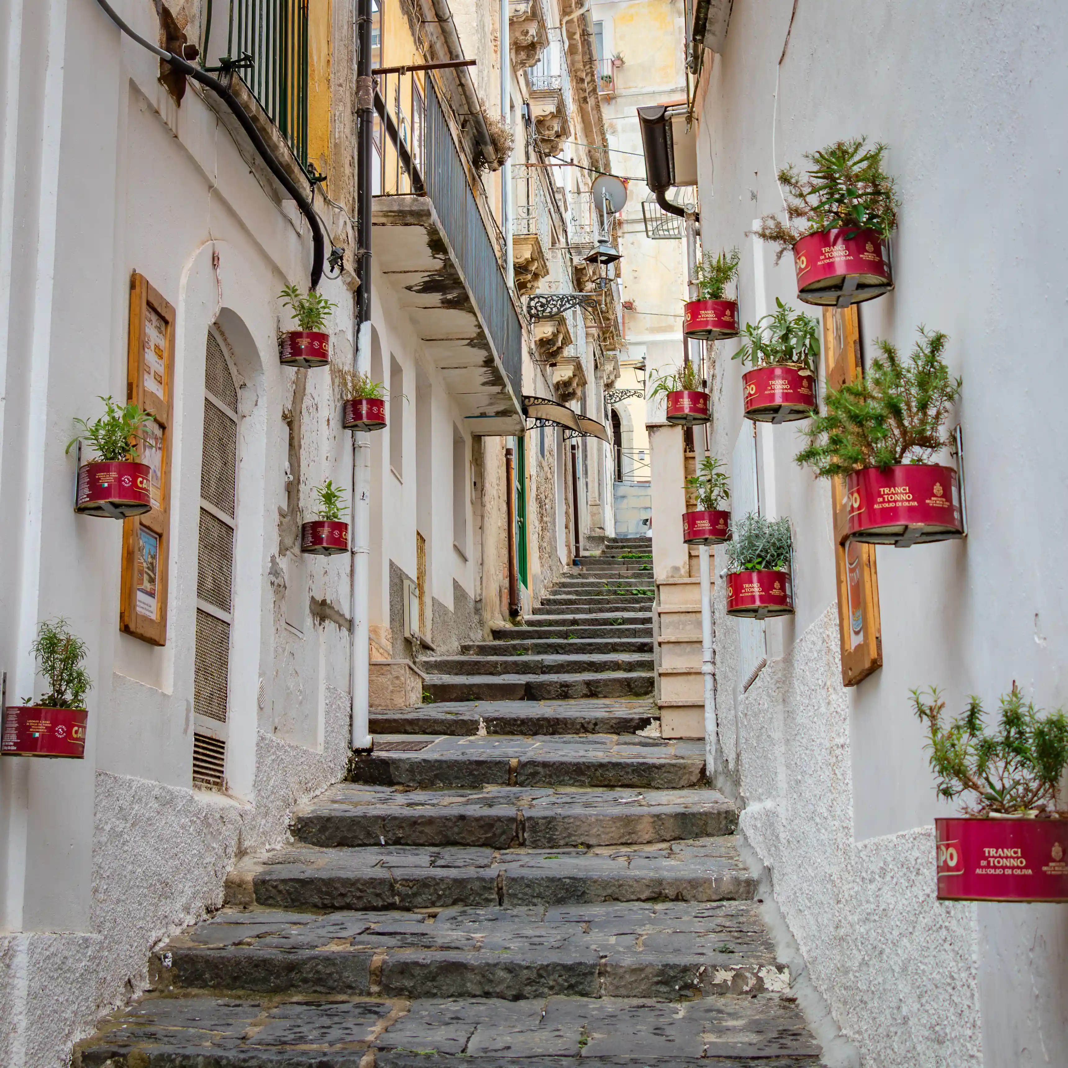 A narrow stone staircase lined with buildings and small red planters mounted along both walls.