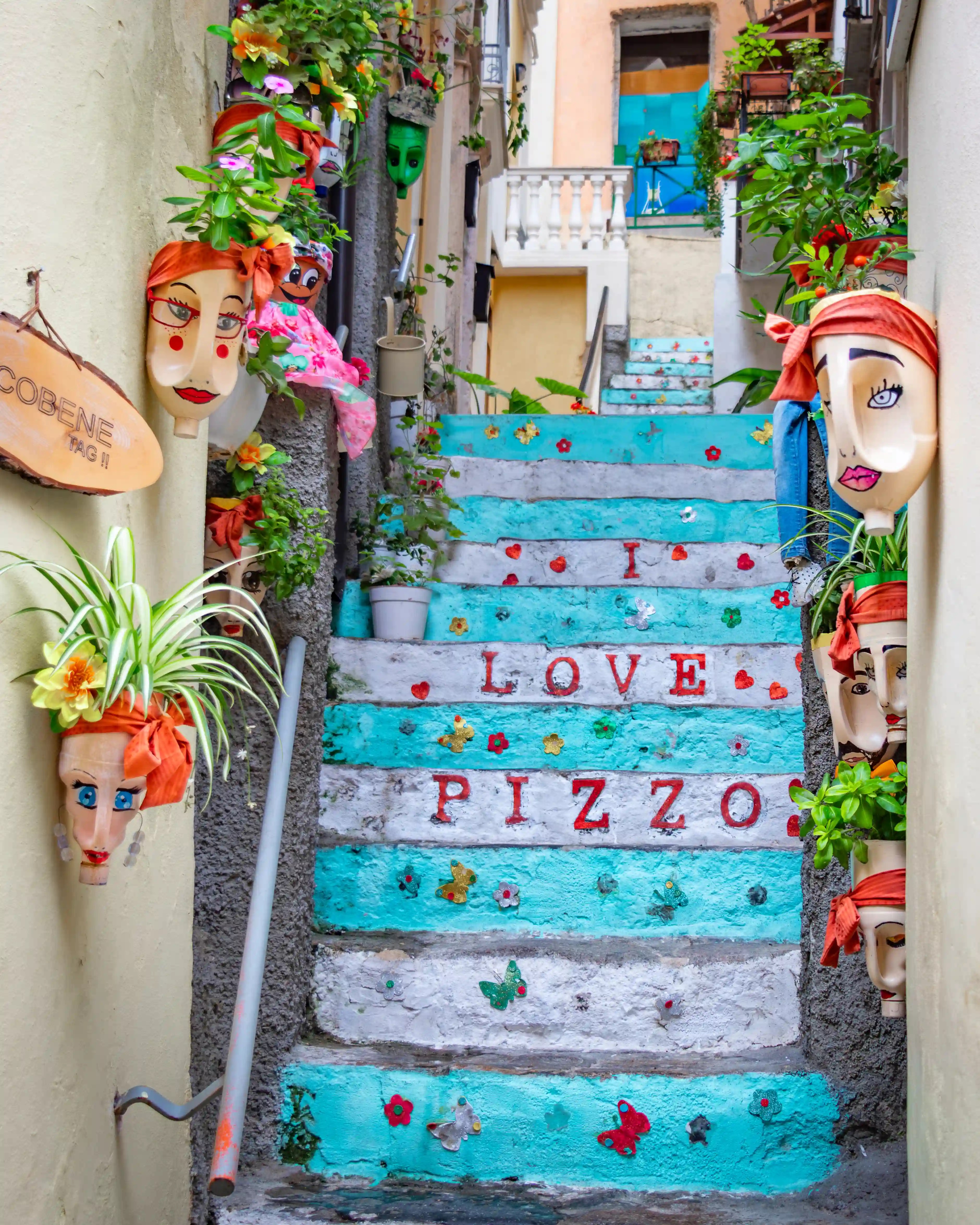 A staircase painted in turquoise and white with decorative masks and plants mounted along the walls.