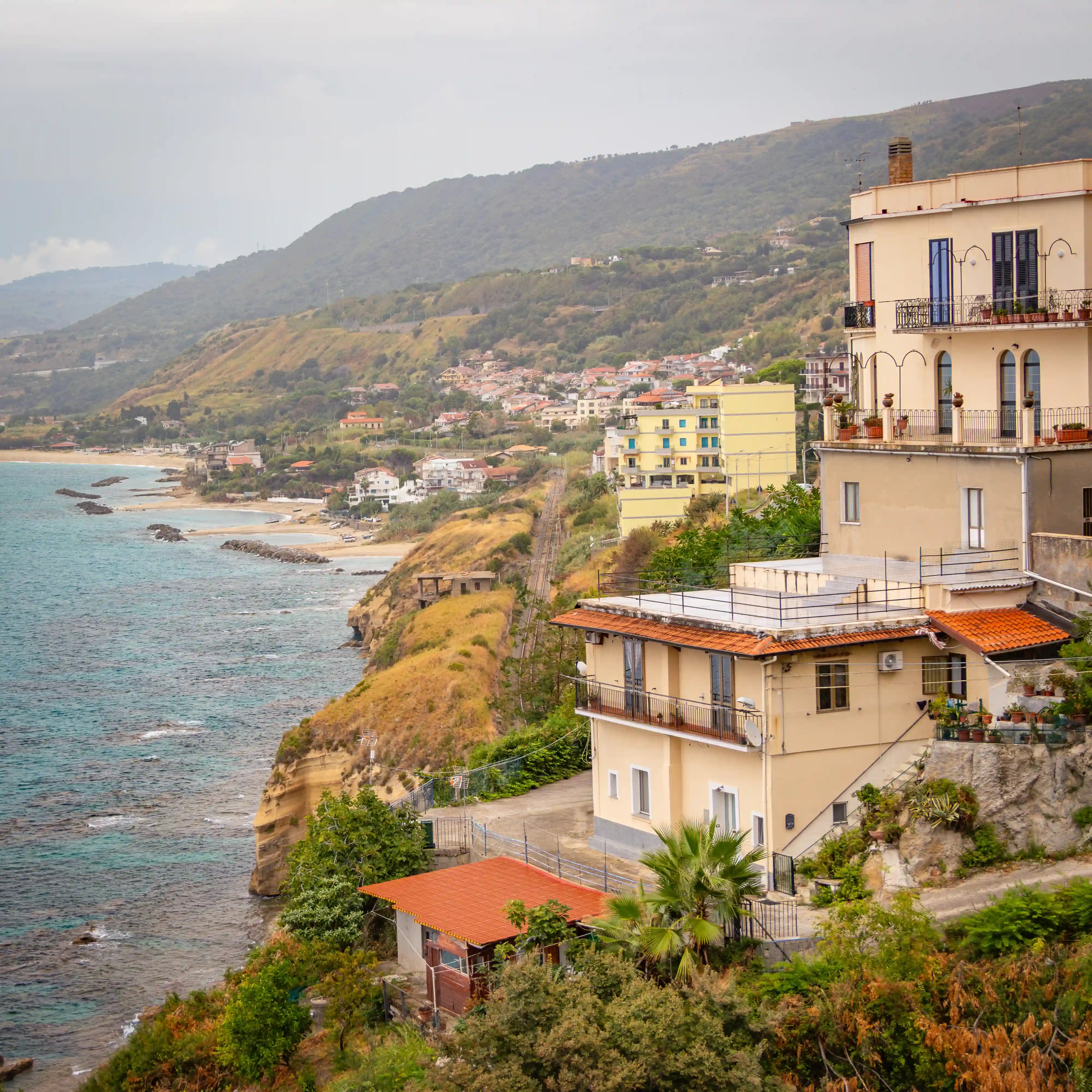 Buildings sit on a cliff above the sea with a railway line running along the coastline below.