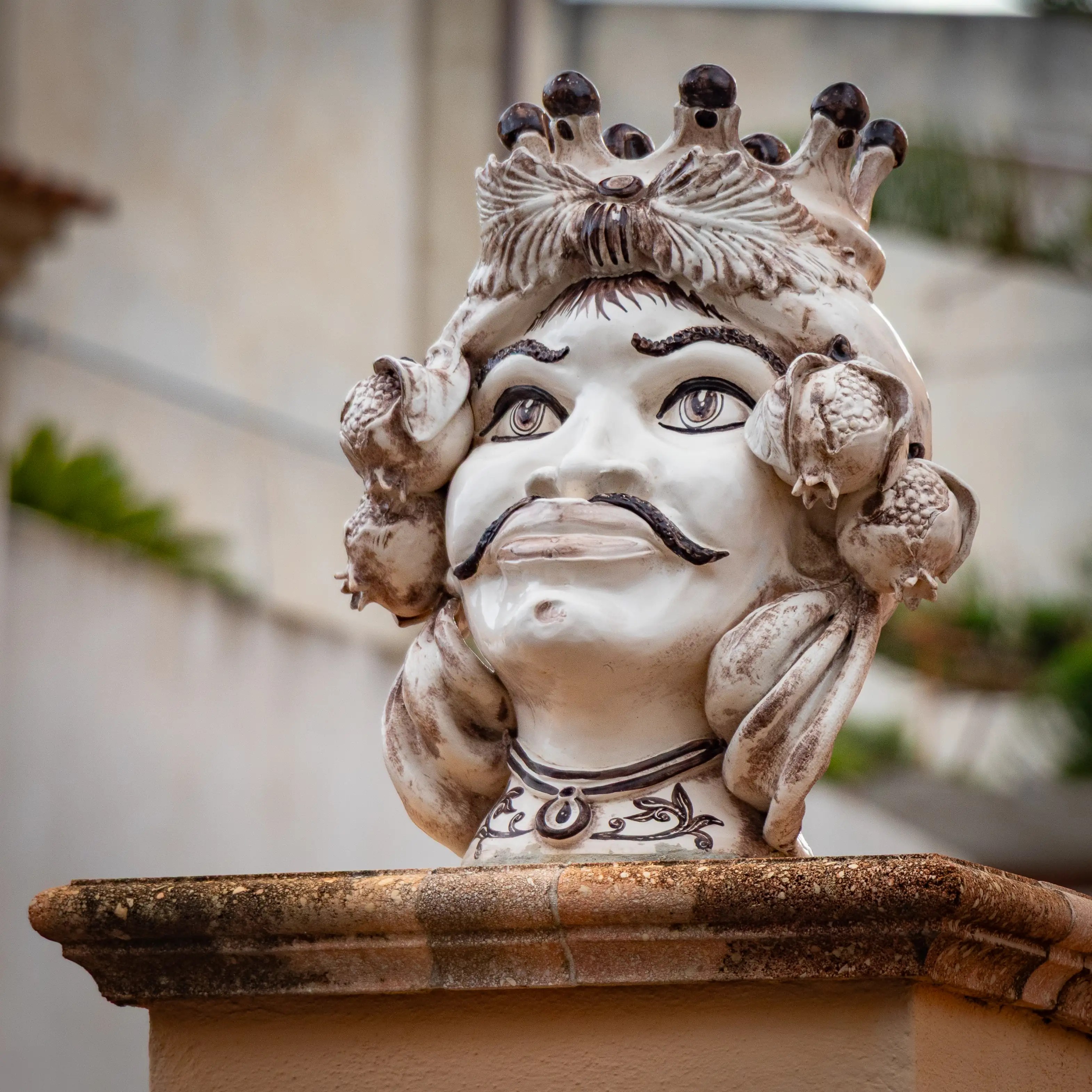 Decorative ceramic head with crown and fruit details placed on a ledge.