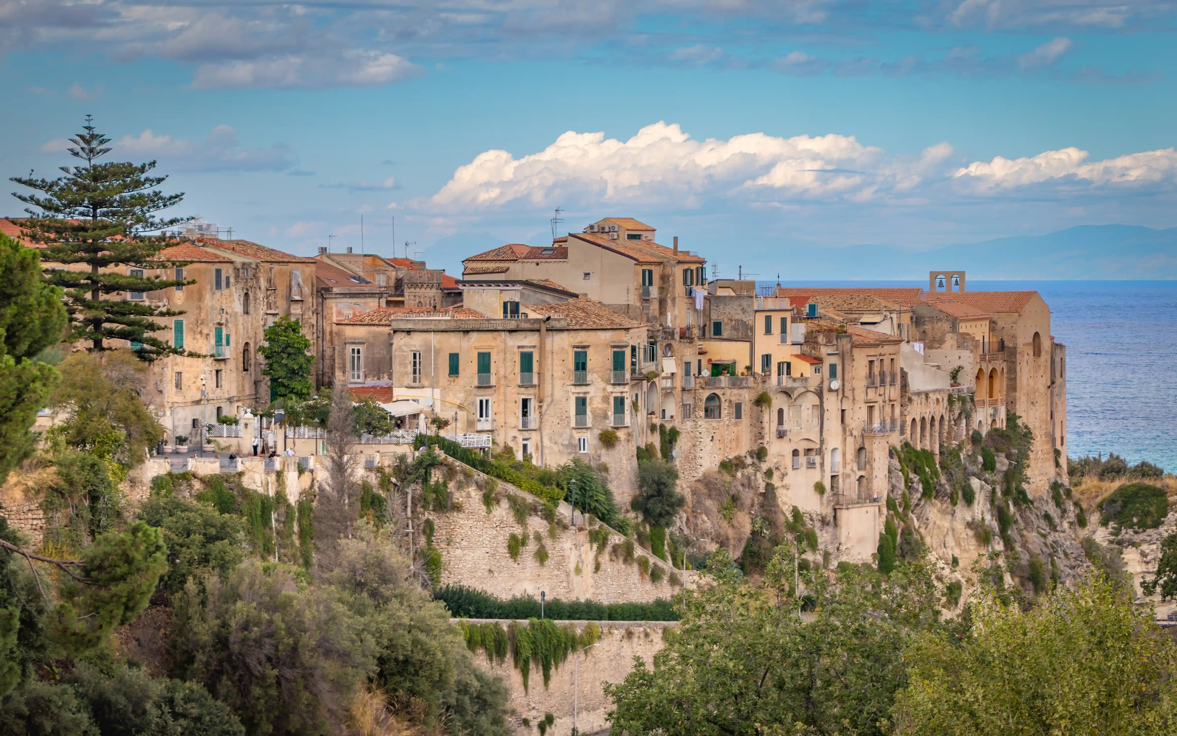 Historic buildings perched on a rocky cliff with greenery below in Tropea.