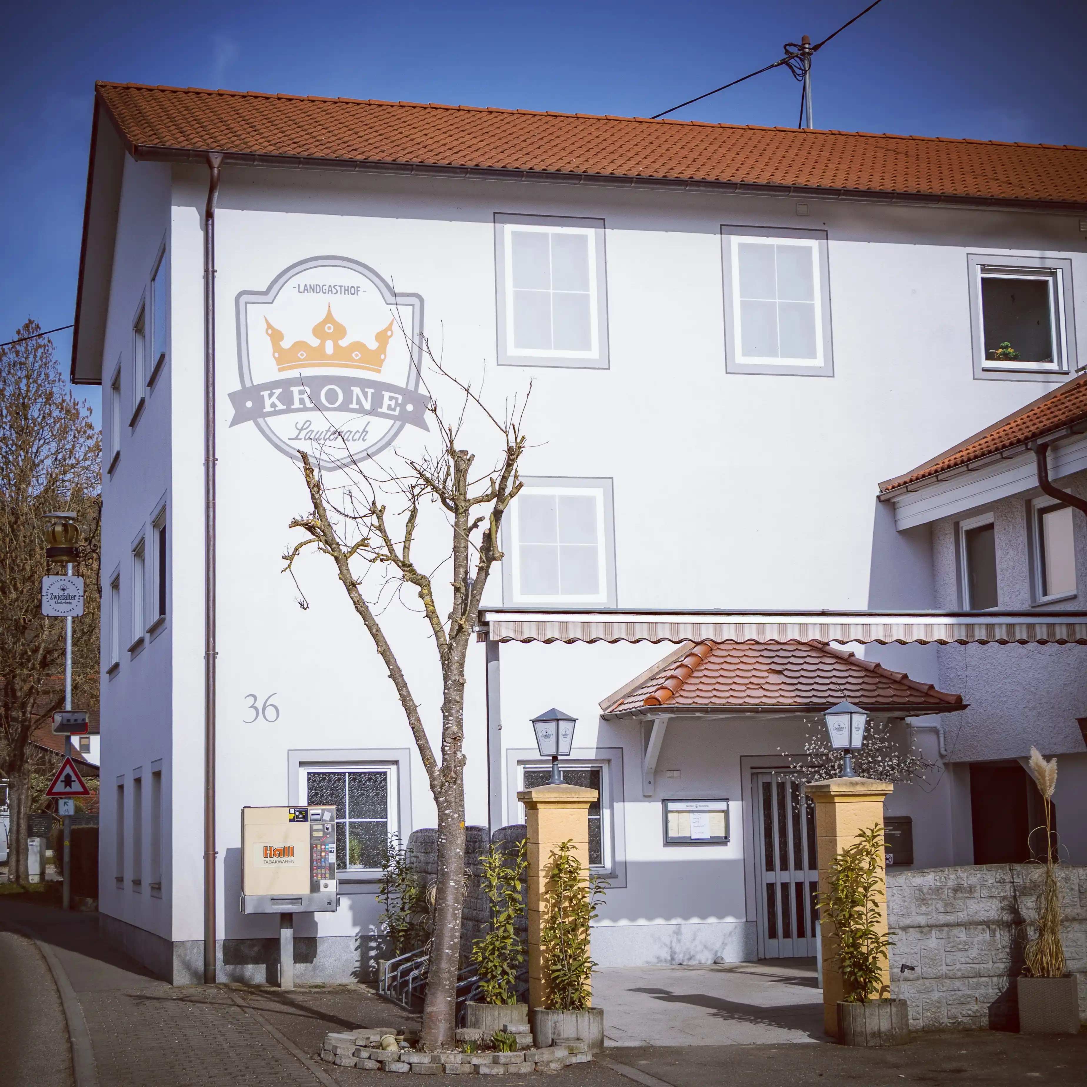 A white building with a red tiled roof and a sign reading “Krone Lauterach” above the entrance.