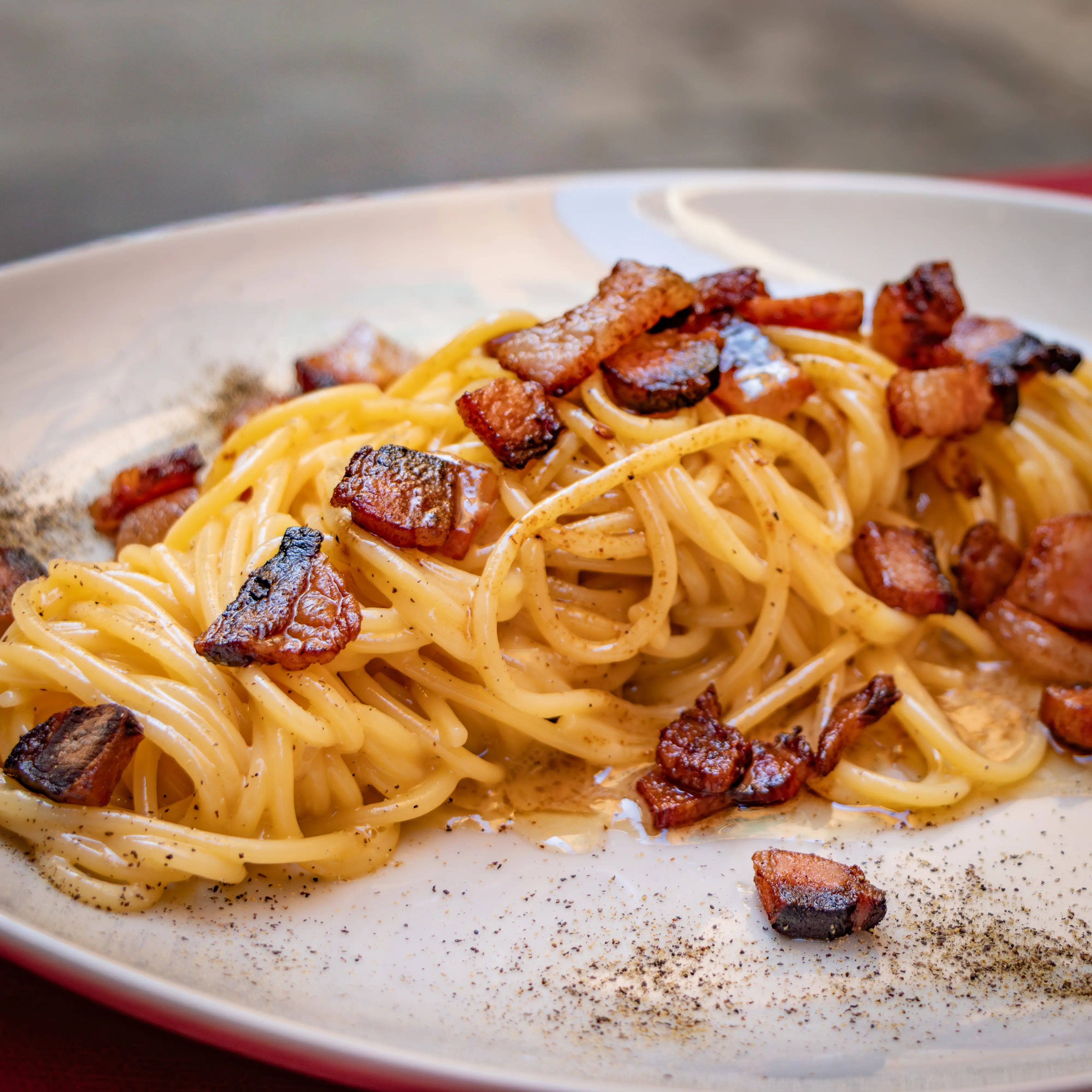 A plate of spaghetti topped with browned pieces of pork and black pepper.
