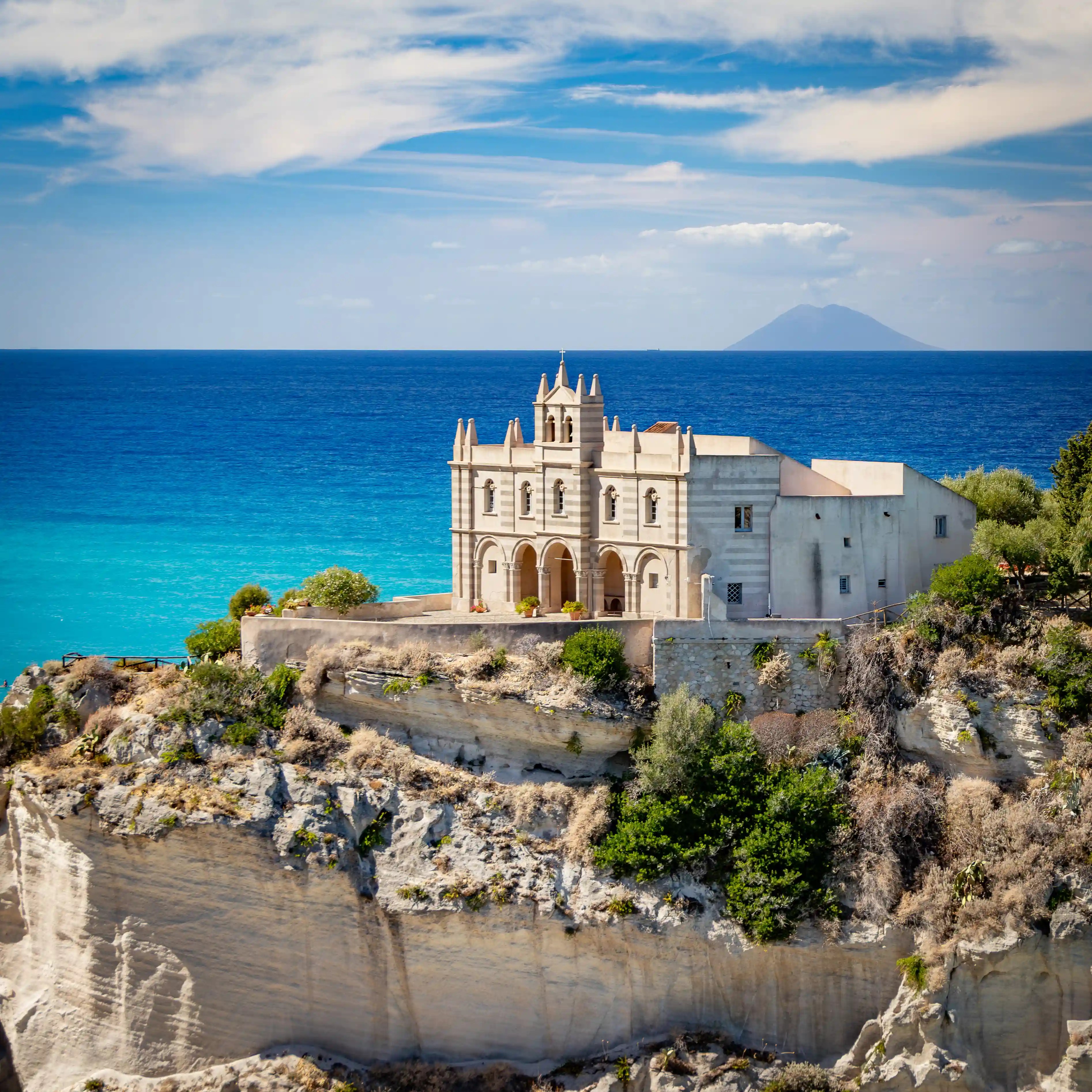 Church building on a rocky cliff above turquoise water with an island visible in the distance.