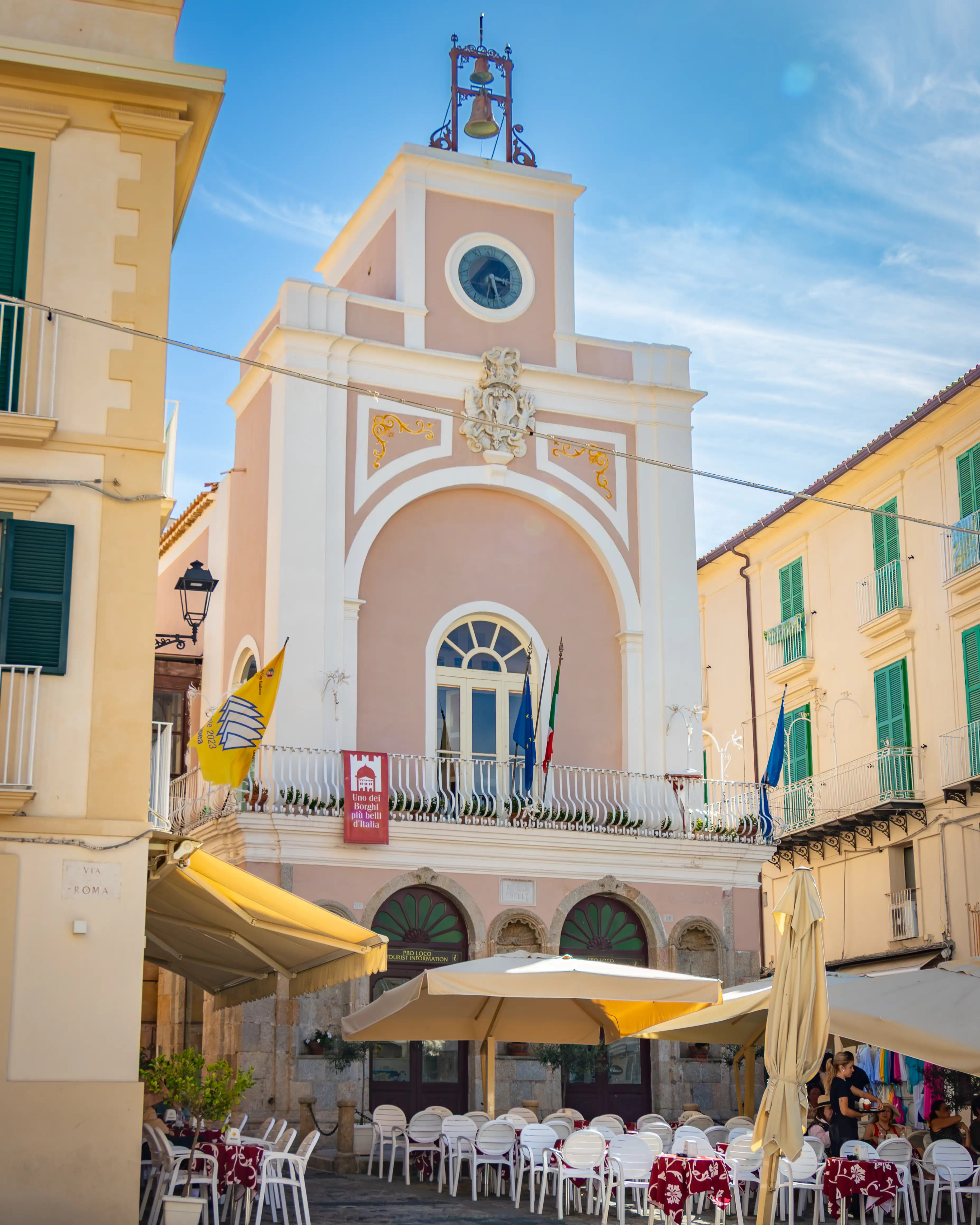 Small square with a pastel-colored building featuring a clock and bell structure above.