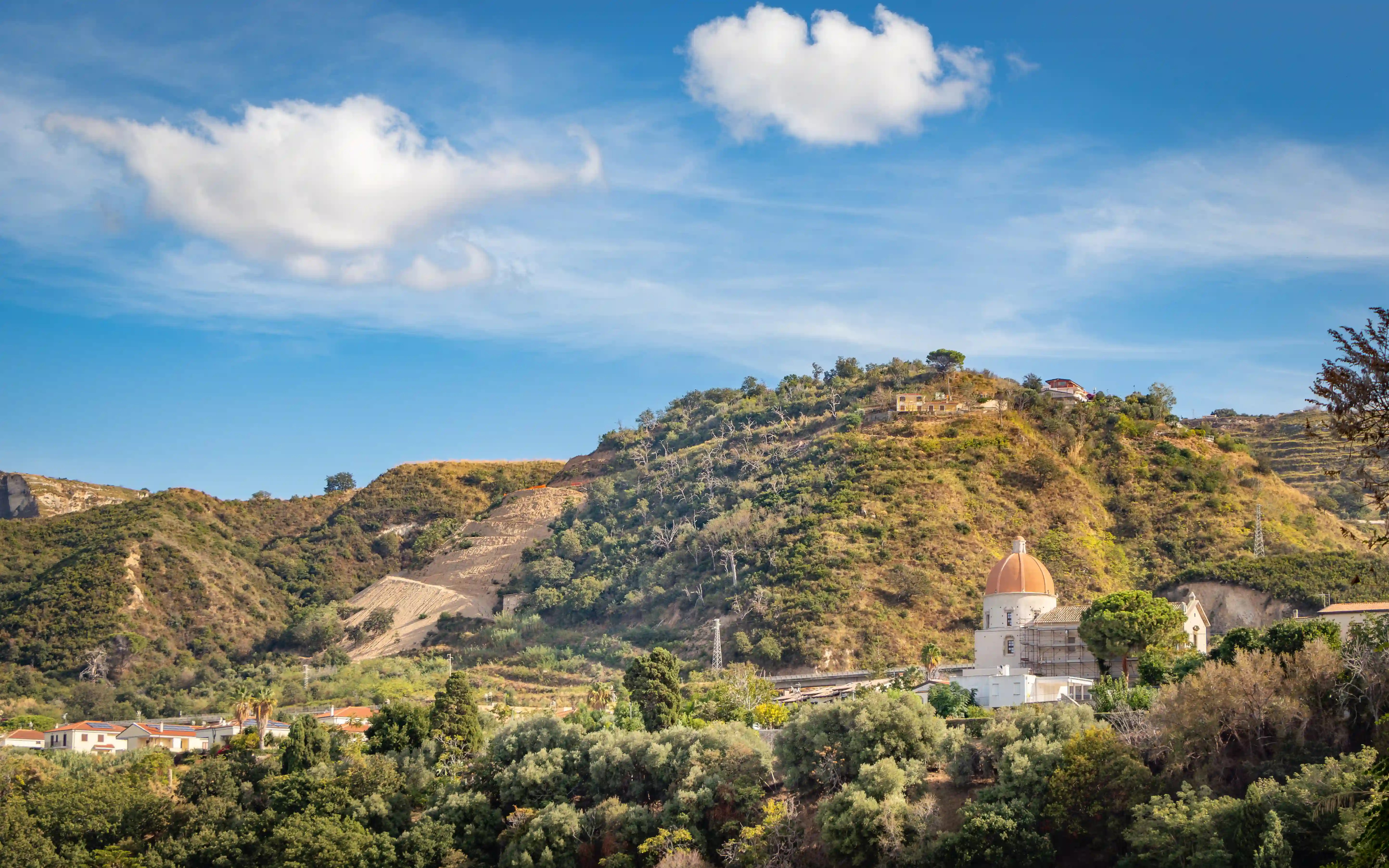 Hill covered with vegetation and buildings, including a structure with a dome.