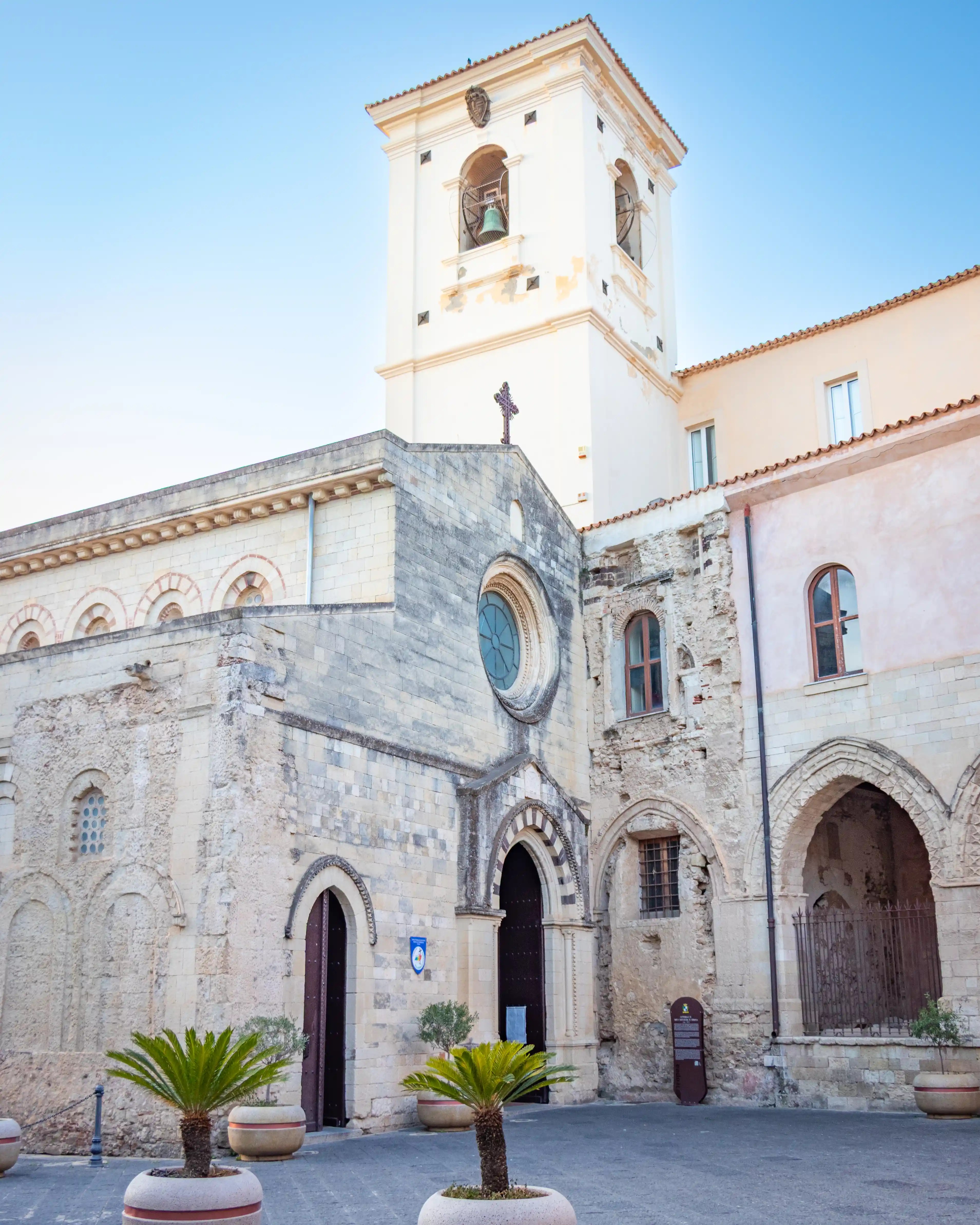 The stone facade of a cathedral with arched doorways, a circular window, and a tall bell tower above.