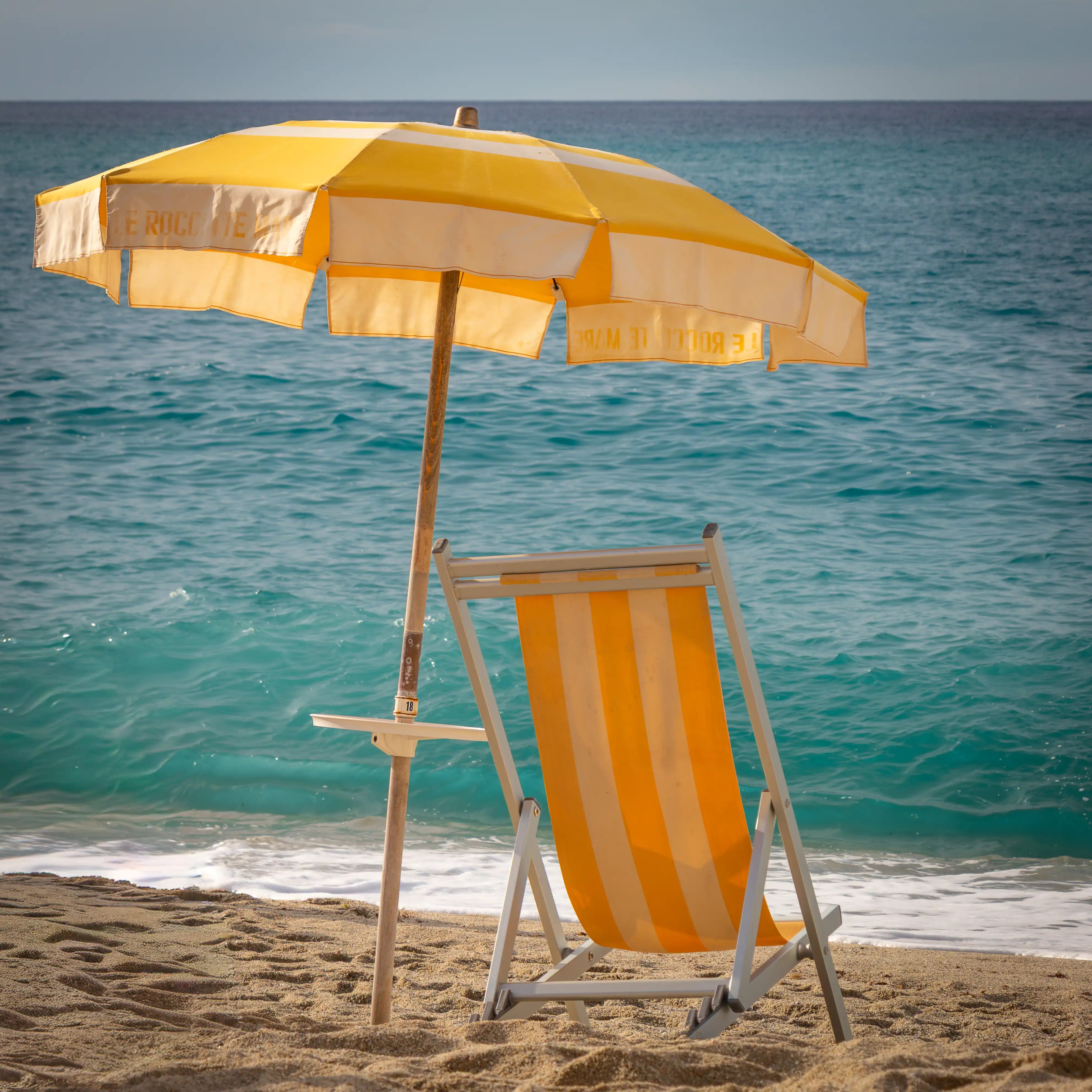 A yellow beach umbrella and matching chair set on sand beside the sea.