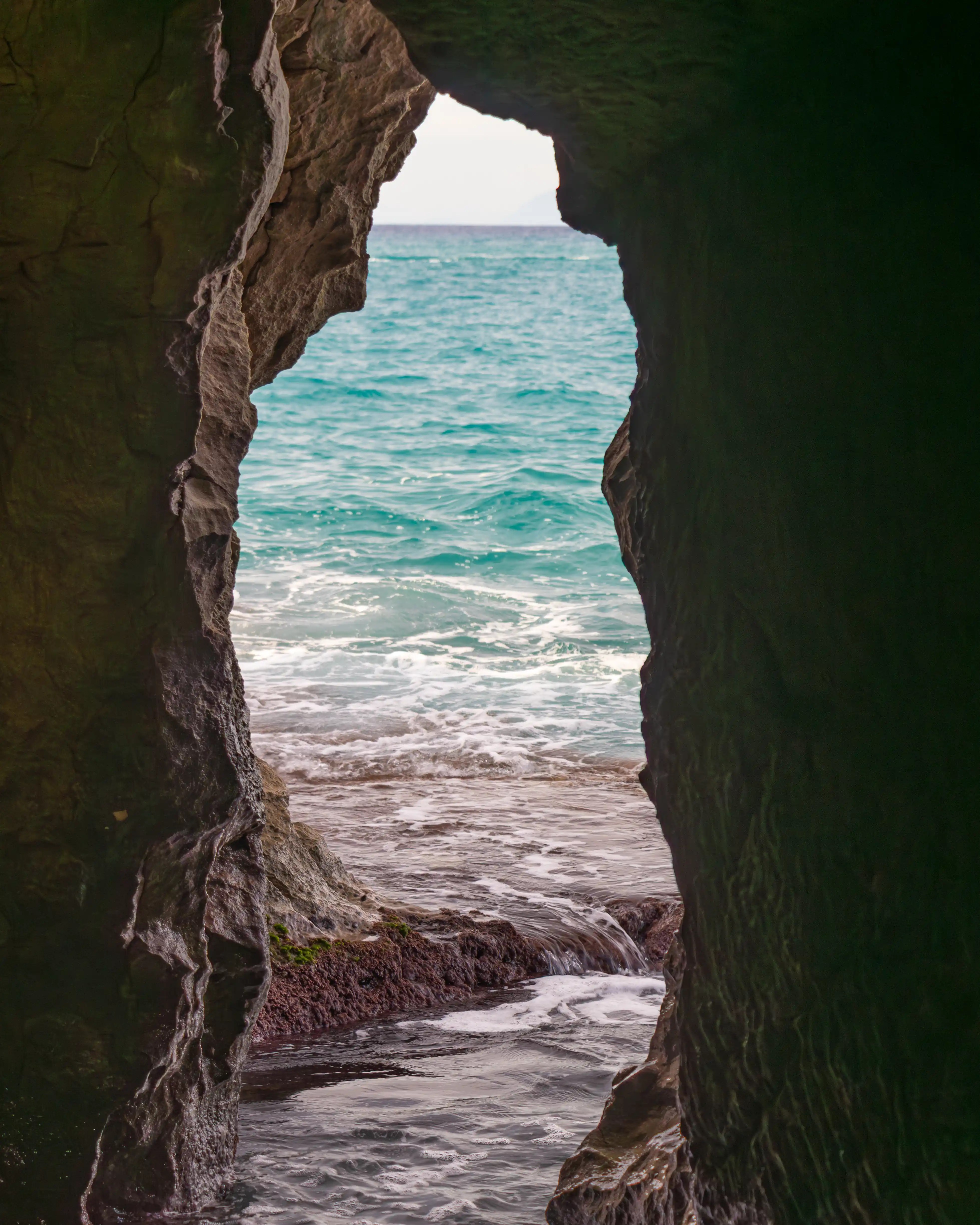A rocky cave opening framing a view of the sea and small waves outside.