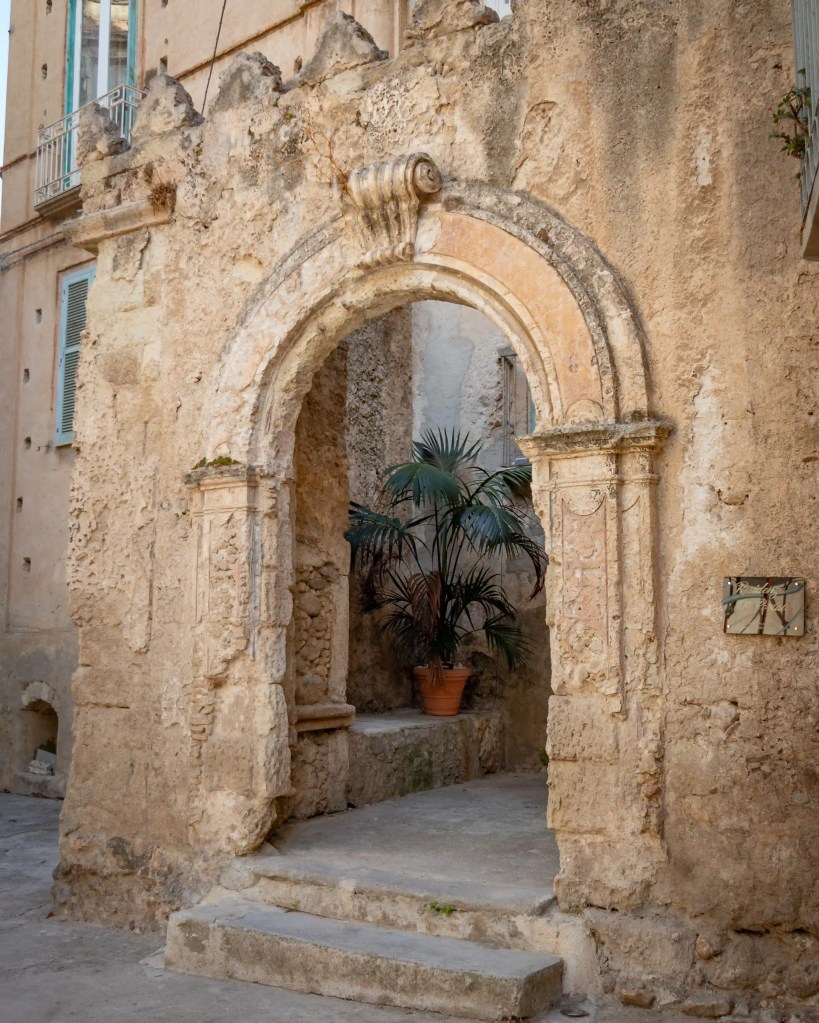 Stone archway with carved details and a small potted plant set inside an opening in a weathered wall.
