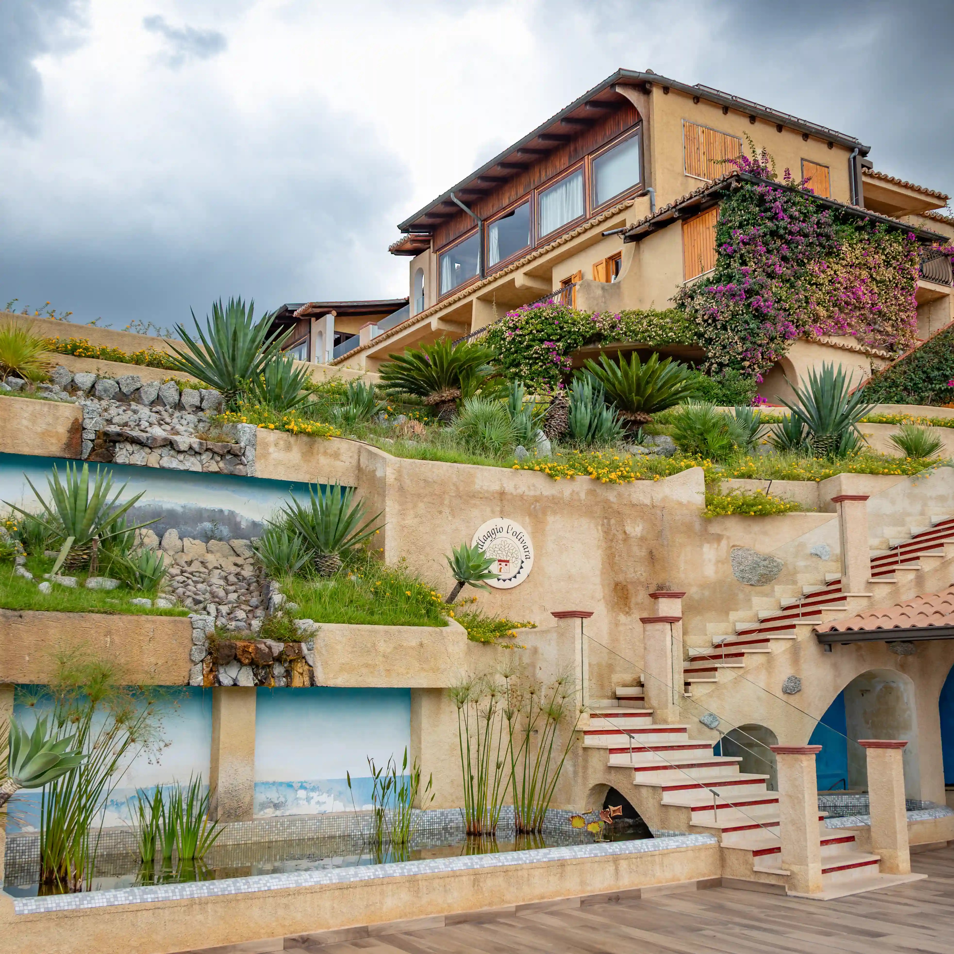 Multi-level building with stairs, terraces, and landscaped plants including agave and flowering vines.