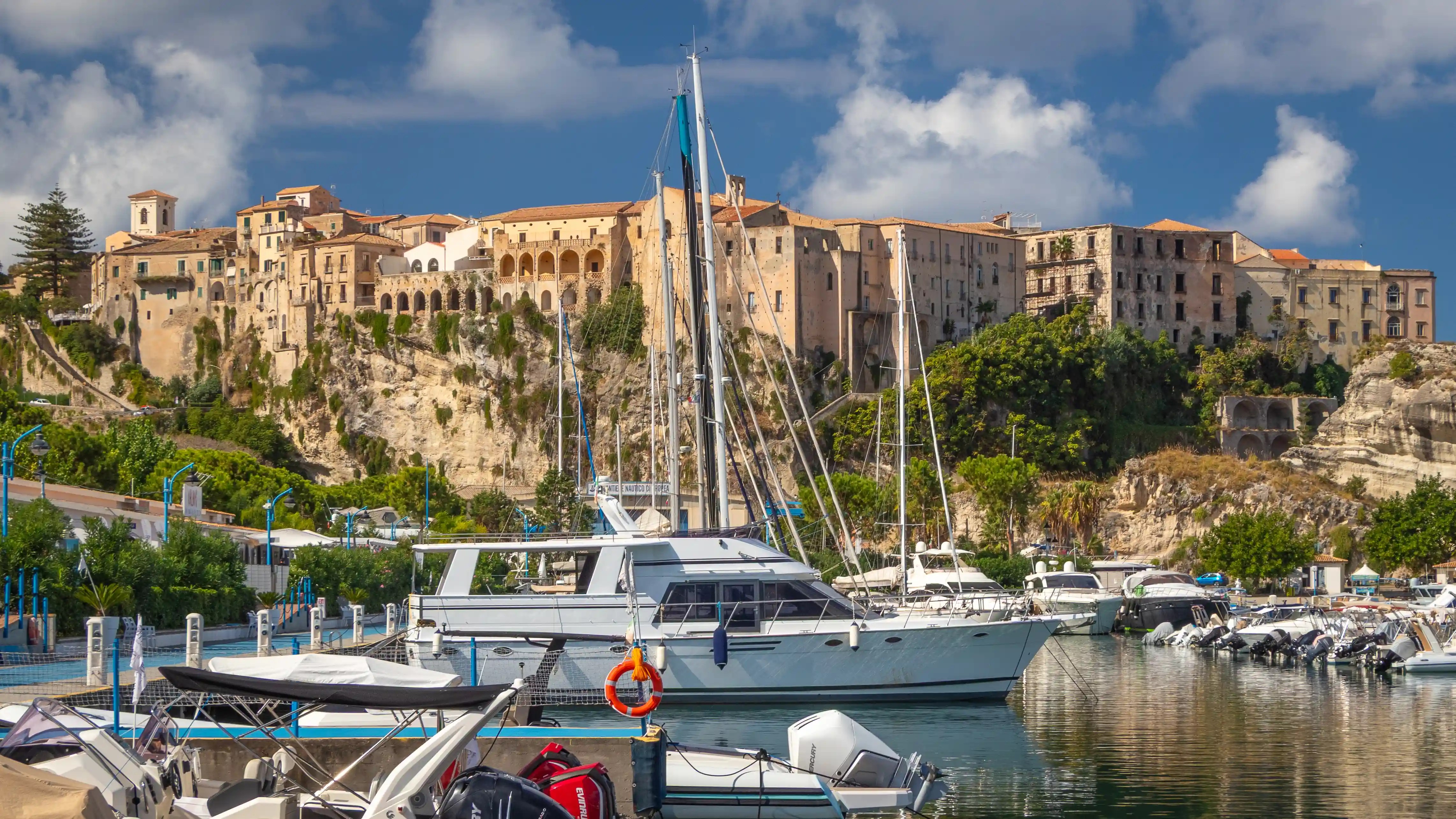 Boats docked in a marina with a town built along cliffs rising in the background.