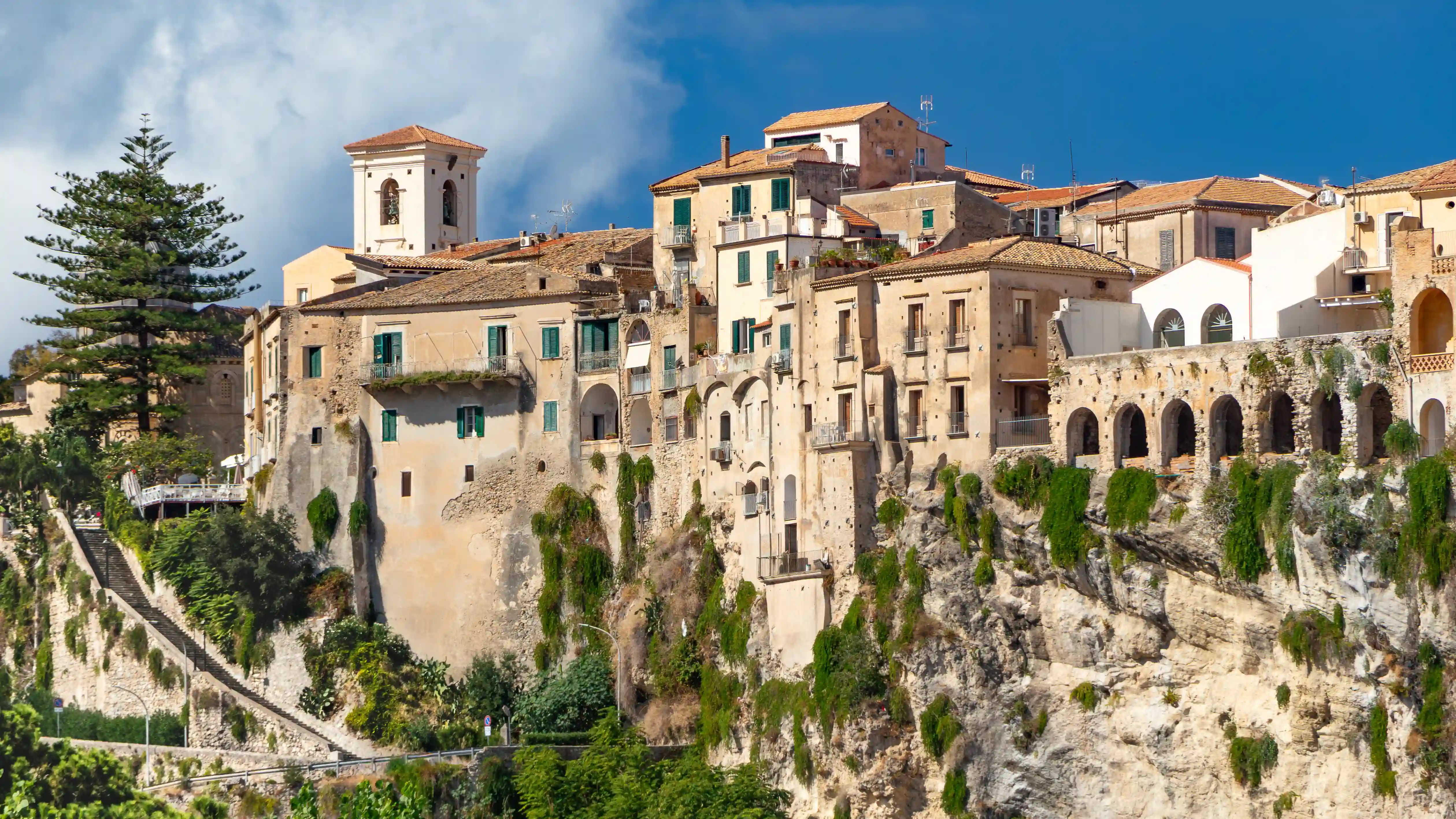 Buildings in Tropea’s historic center perched directly on a rocky cliff with greenery growing along the stone.