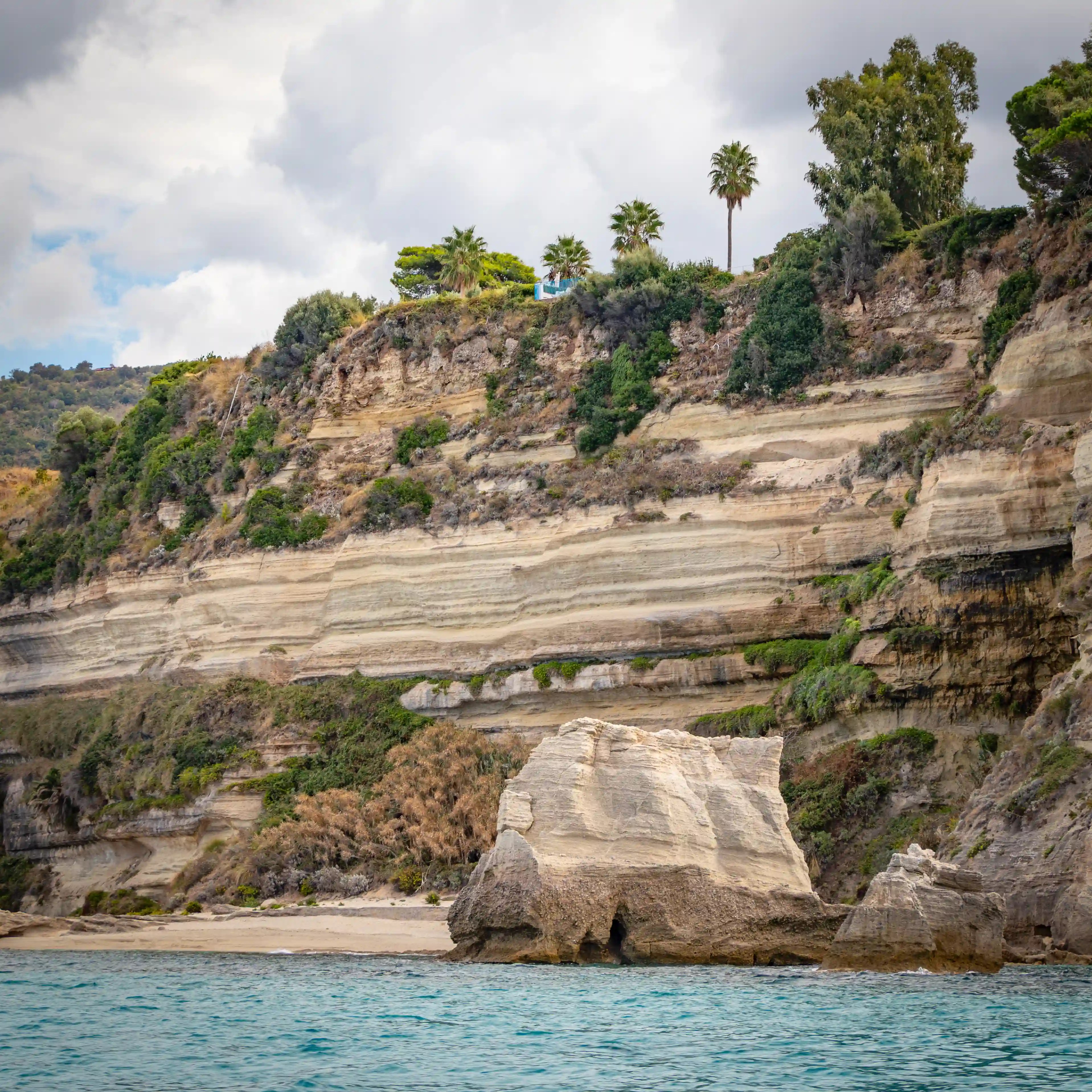 Layered coastal cliffs with horizontal bands of rock and trees growing along the top edge above the sea.