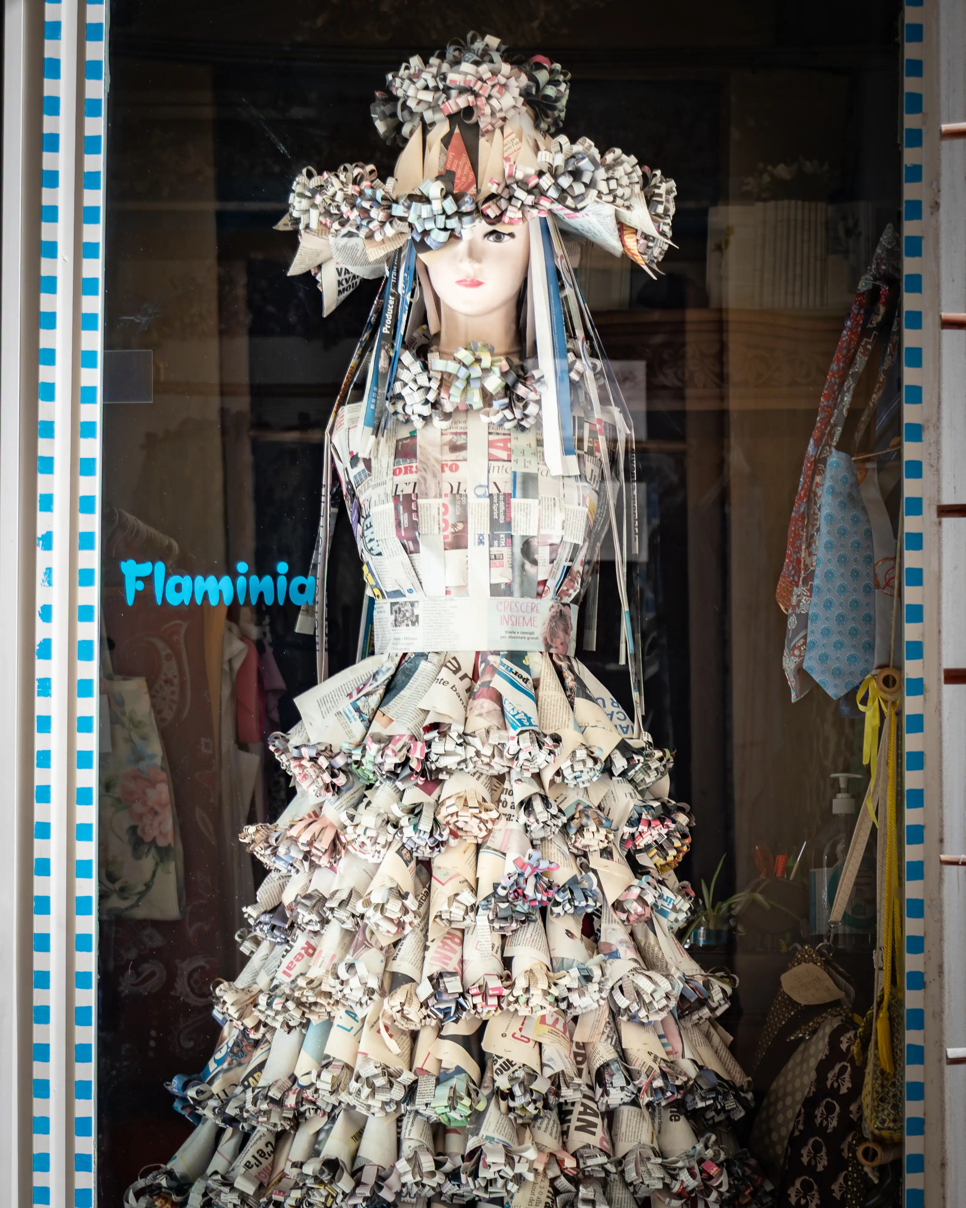 A mannequin wearing a dress and hat made from folded paper displayed in a shop window.
