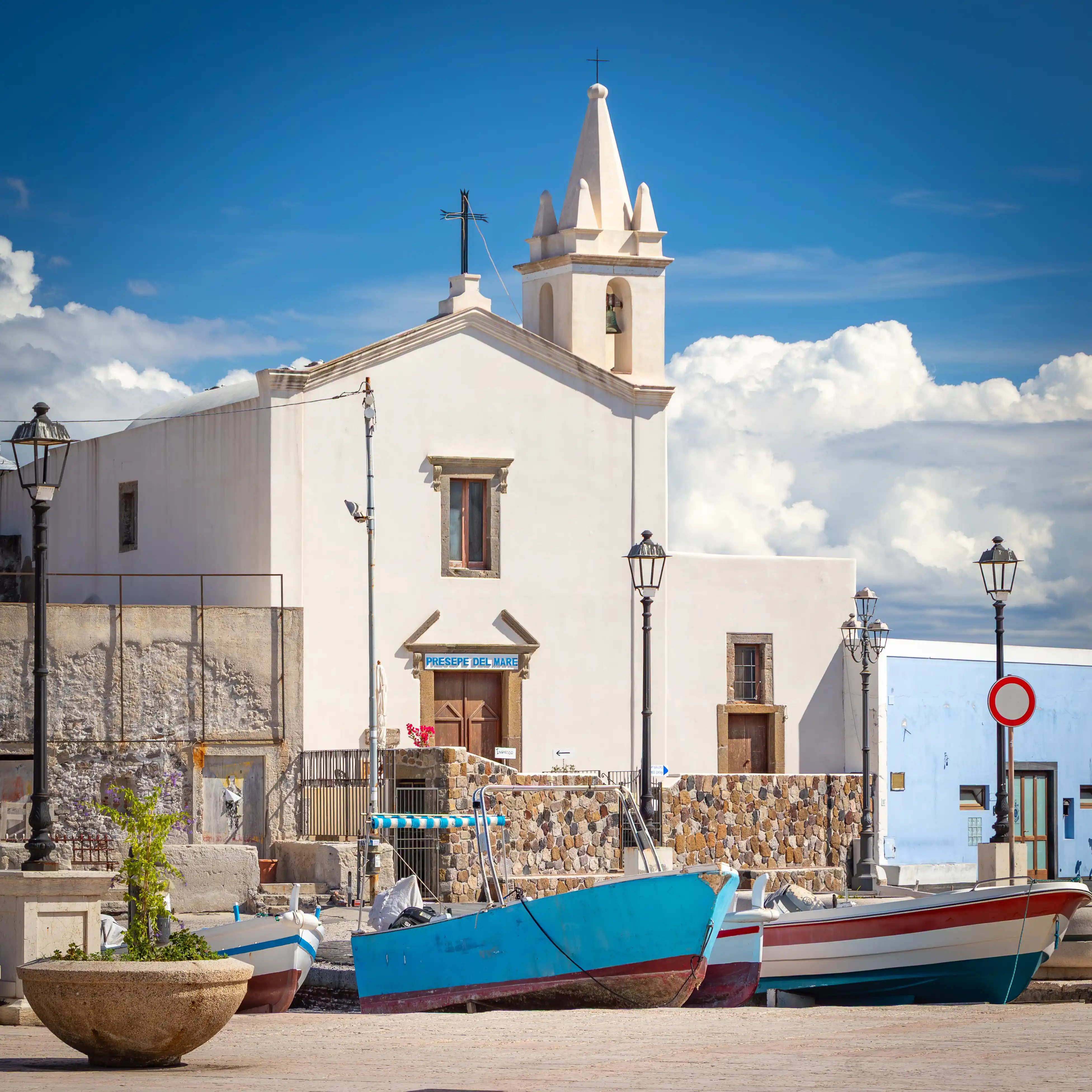 A white church with a bell tower beside small boats docked along a waterfront.