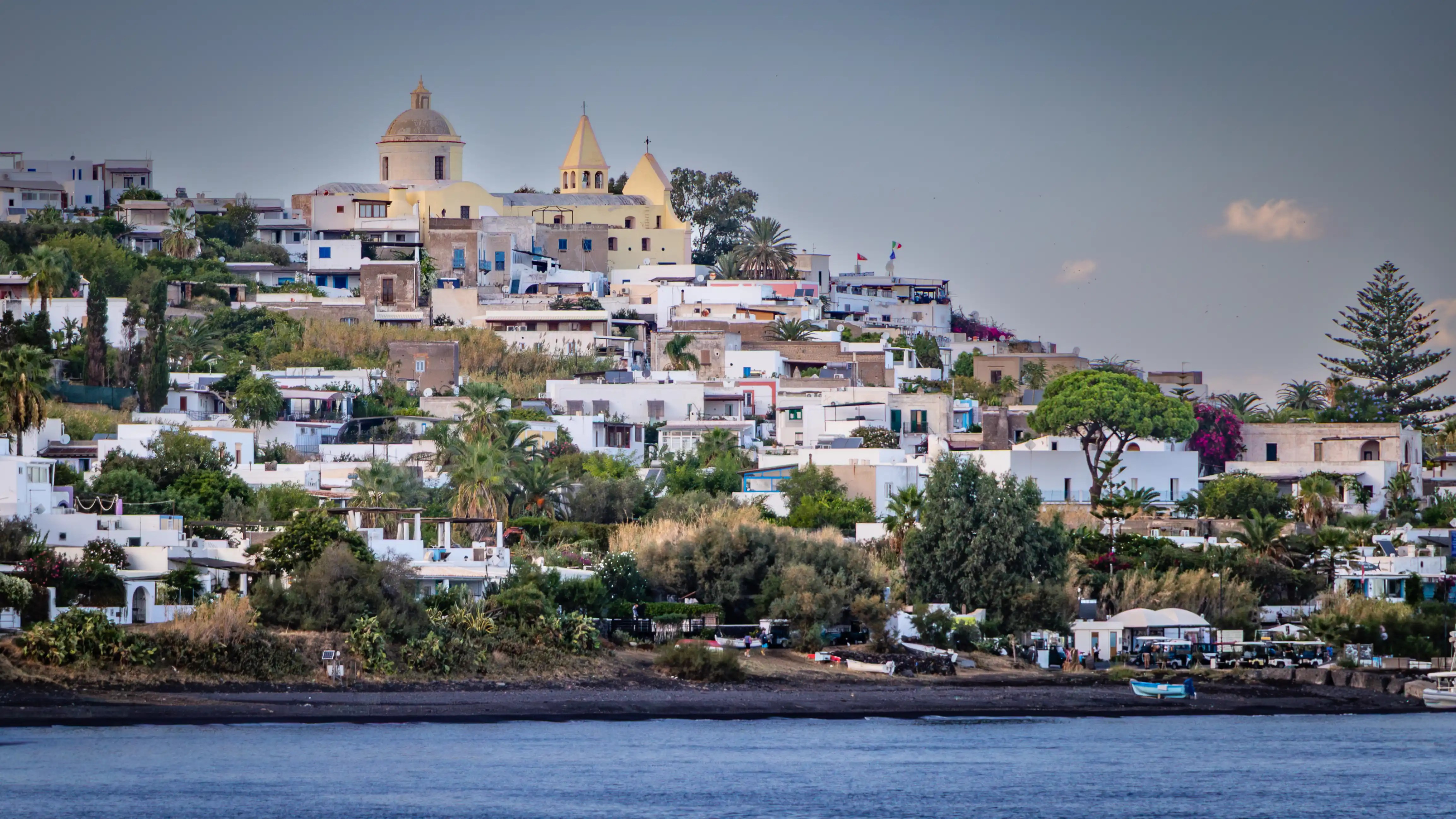 A hillside village with white buildings and a church complex with domes and towers above them.